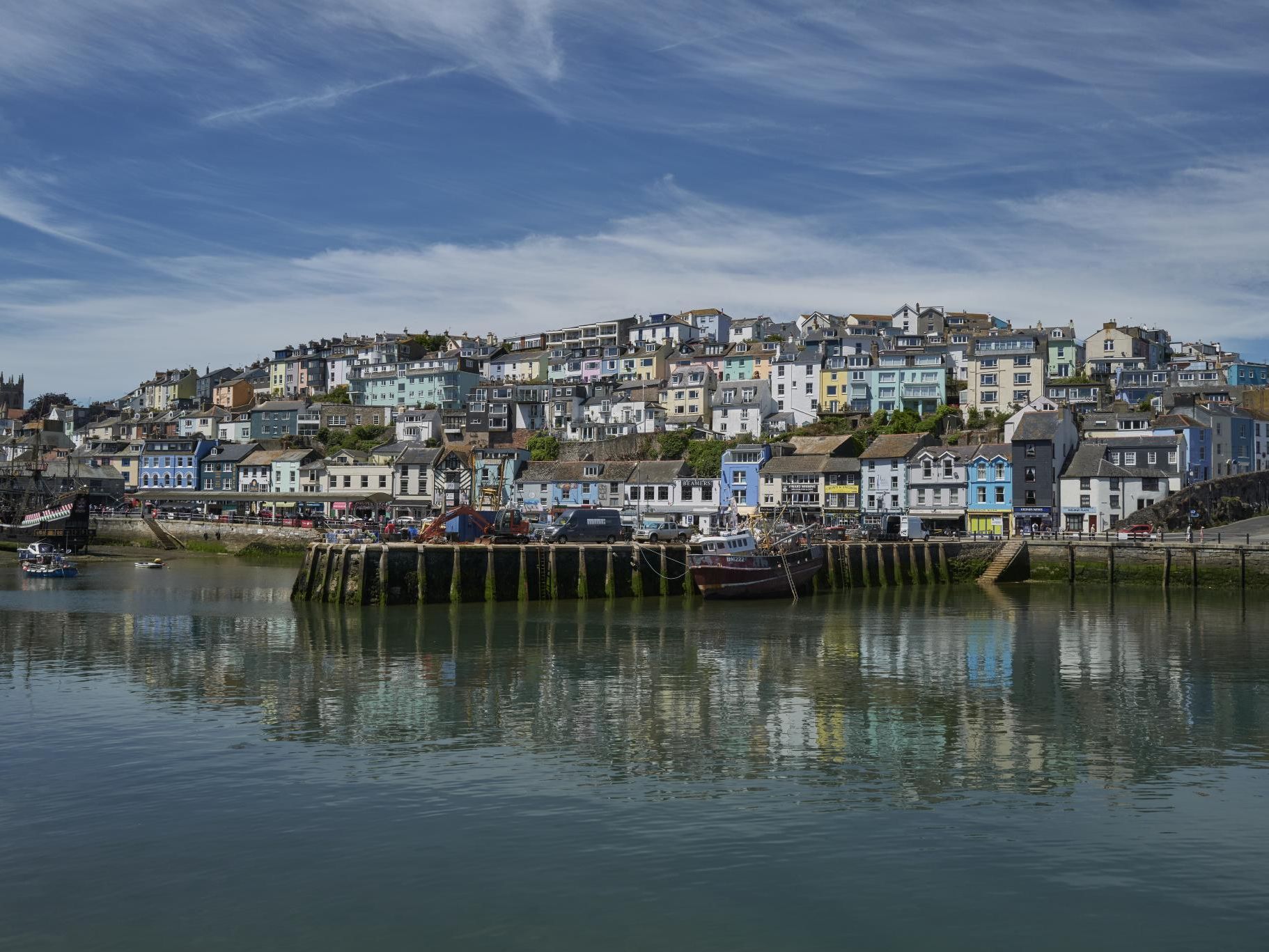 Colourful hillside houses overlooking a harbour with calm water reflections under a blue sky