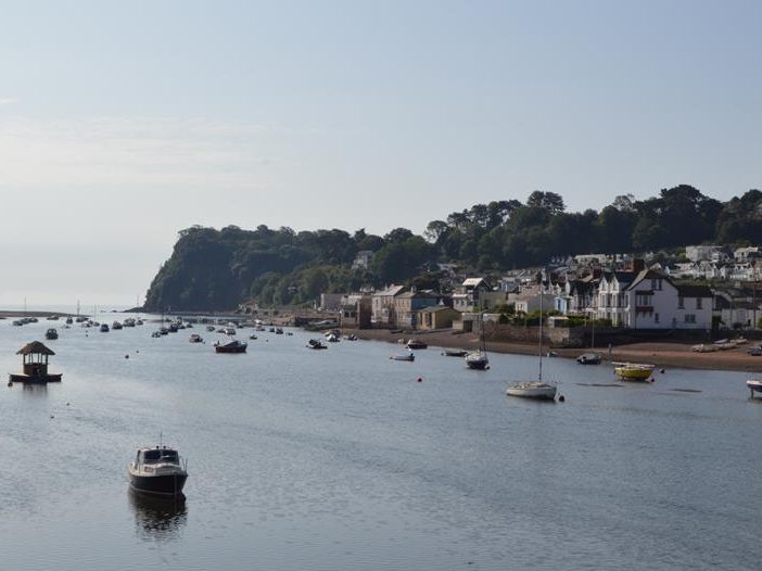 Boats moored on the calm harbour at Shaldon with a row of seaside houses along the shoreline