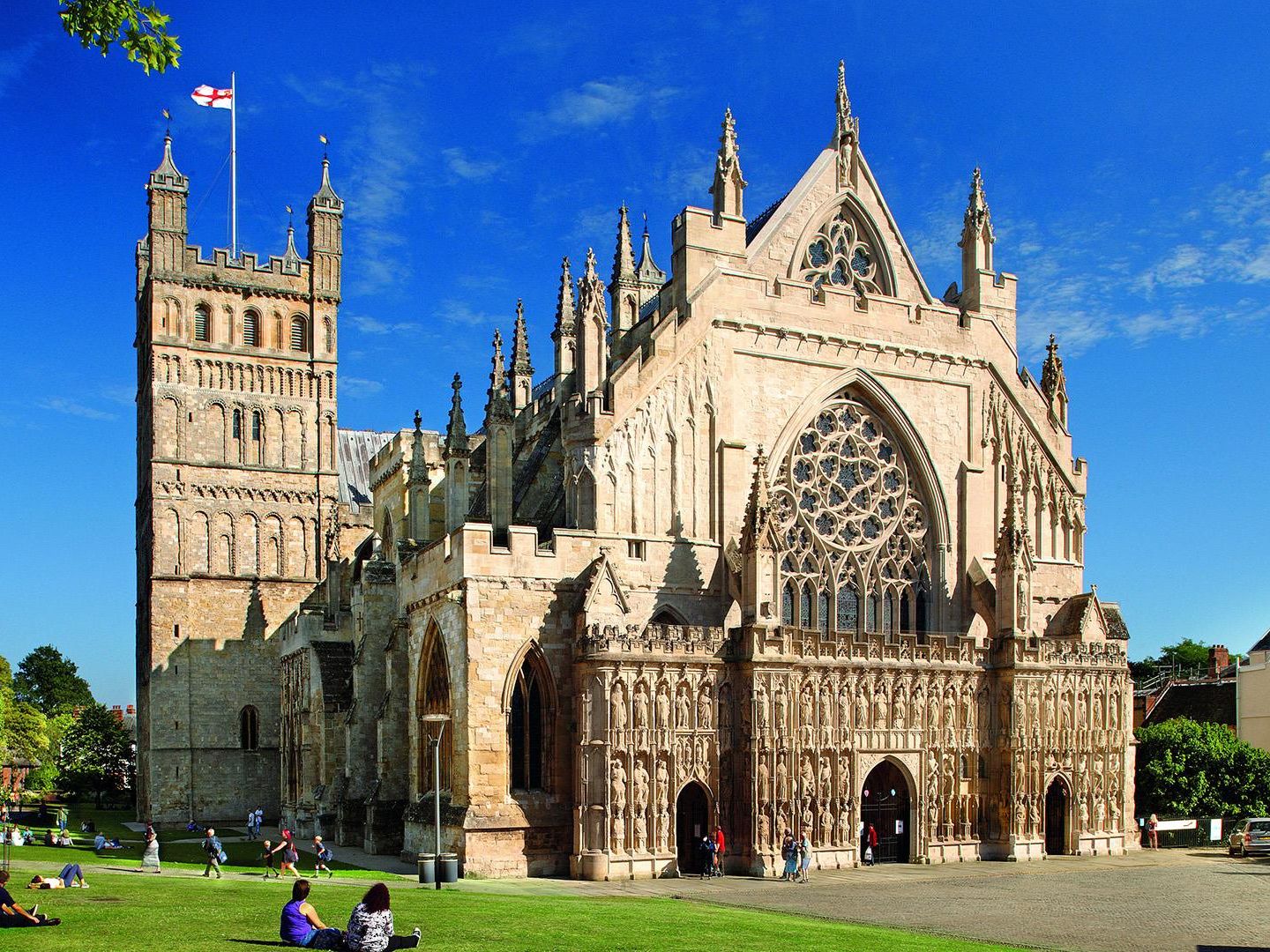 Exeter Cathedral in Devon, England, with people on the green under a bright blue sky