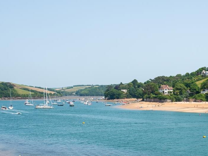 Sailboats moored in a calm estuary beside a sandy beach and green hills at Salcombe.
