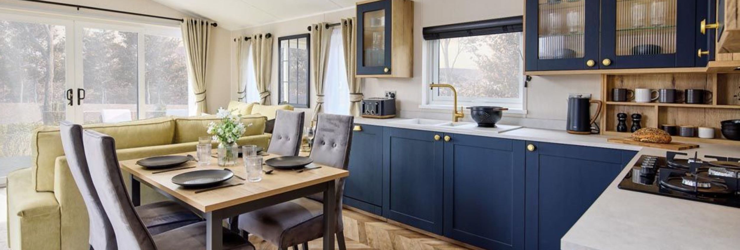 Modern open-plan kitchen and dining area with navy cabinets, wooden table and grey chairs