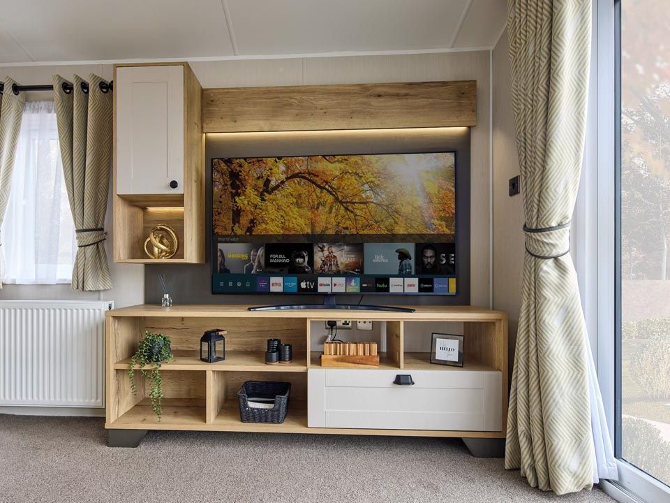 Modern living room TV unit with wood and cream cabinetry, shelves and patterned curtains