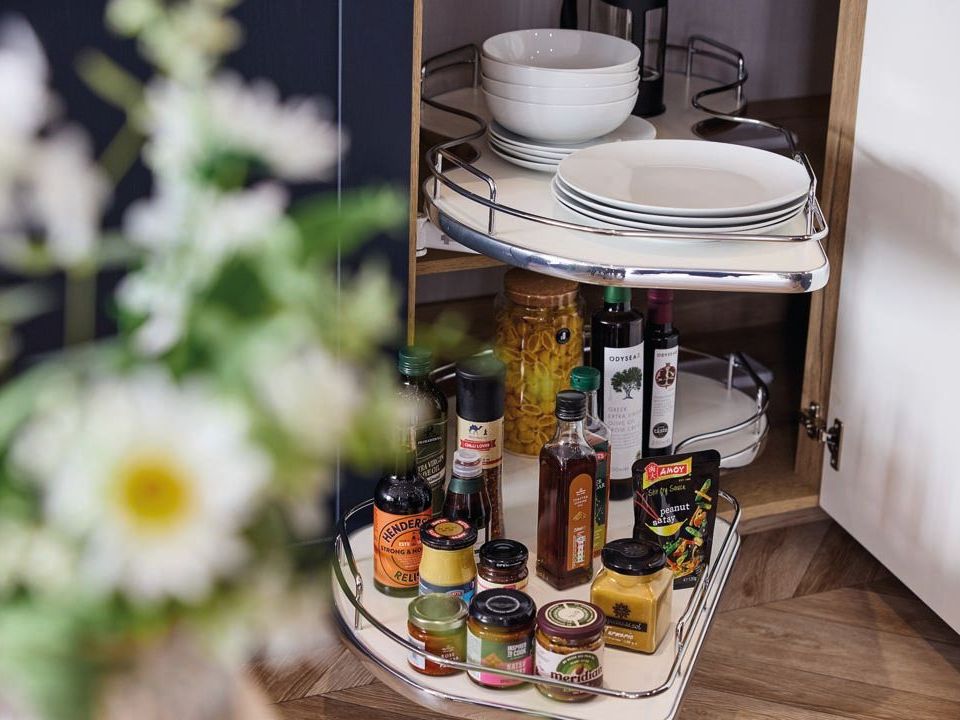 Corner kitchen cupboard with pull-out shelves holding plates, bowls, bottles and jars
