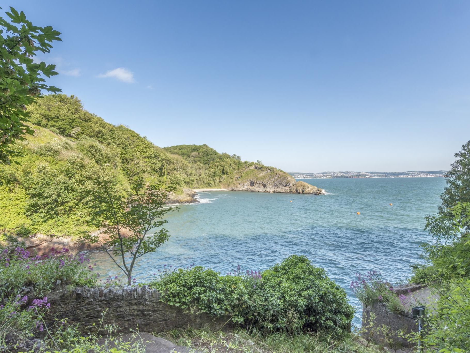 Coastal view of a sheltered bay with wooded cliffs and calm blue sea under a clear sky