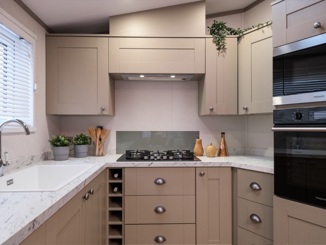 Modern L-shaped kitchen with beige cabinets, marble-effect worktop, gas hob and built-in double oven