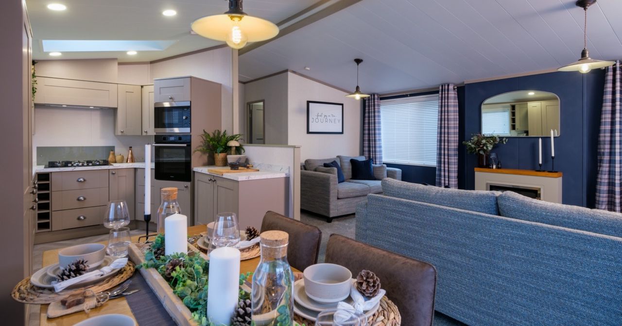 Open-plan kitchen, dining and lounge area with grey cabinetry, set dining table and blue accent wall