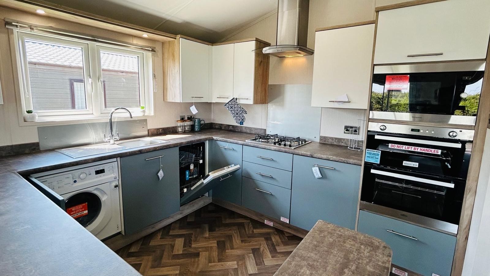 Modern L-shaped kitchen with blue-grey cabinets, white wall units, built-in oven, hob and sink under a window