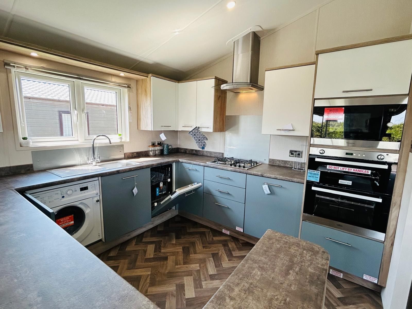 Modern L-shaped kitchen with blue-grey cabinets, white wall units, built-in oven, hob and sink under a window