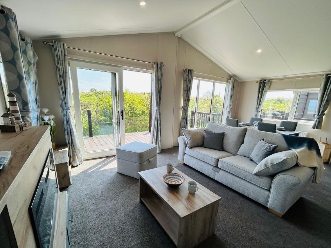 Modern living room with grey sofa, coffee table and large patio doors opening onto a deck