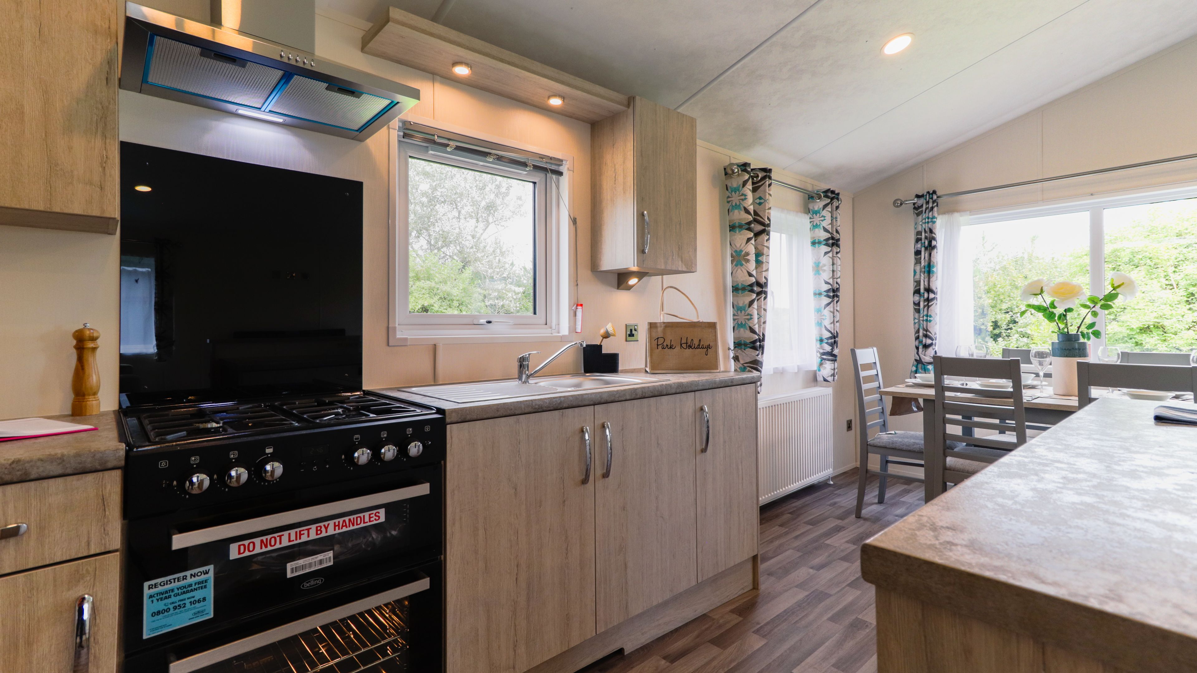 Modern kitchen with black cooker, wooden cabinets, sink and a small dining table by a bright window