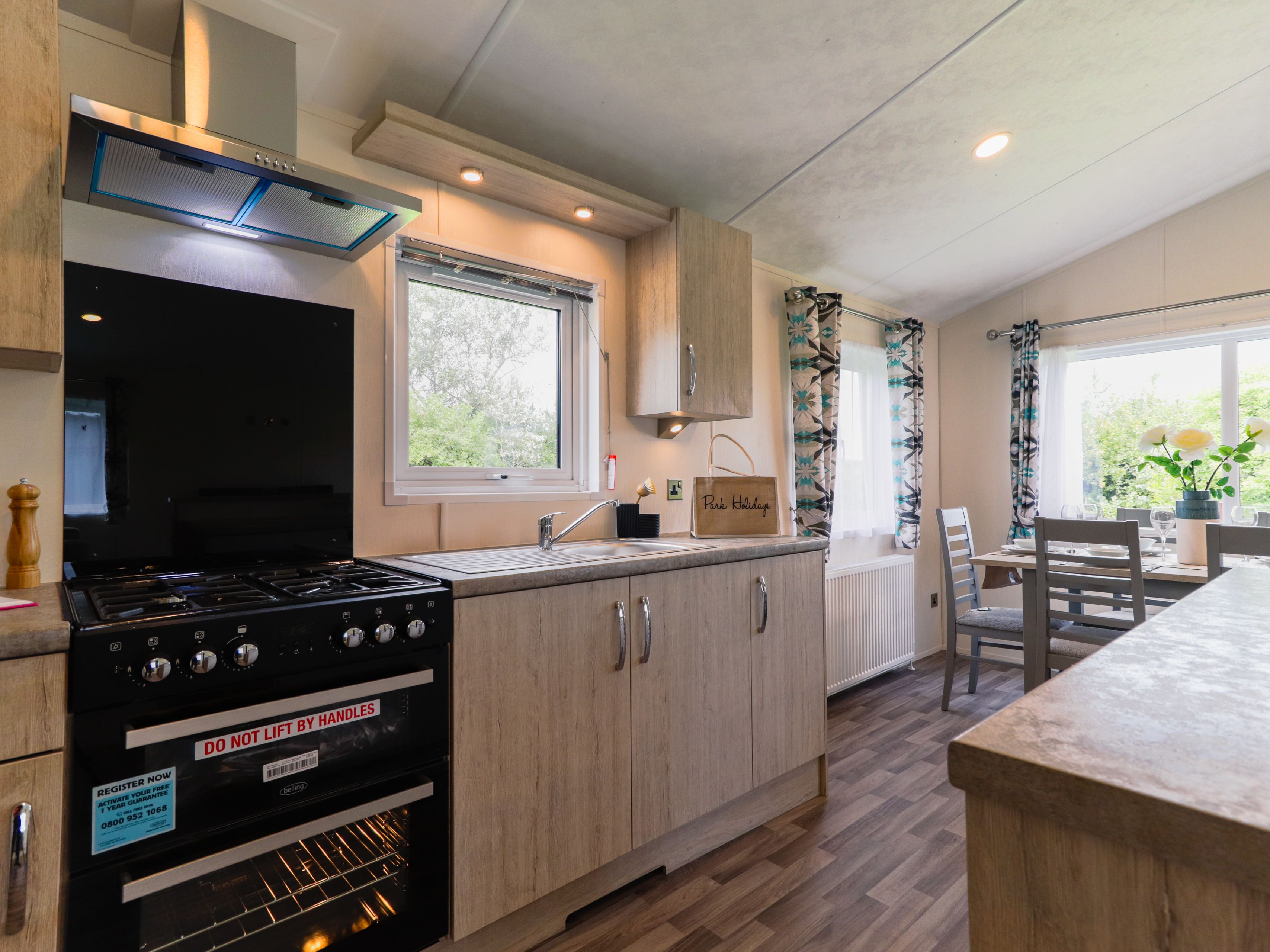 Modern kitchen with black cooker, wooden cabinets, sink and a small dining table by a bright window
