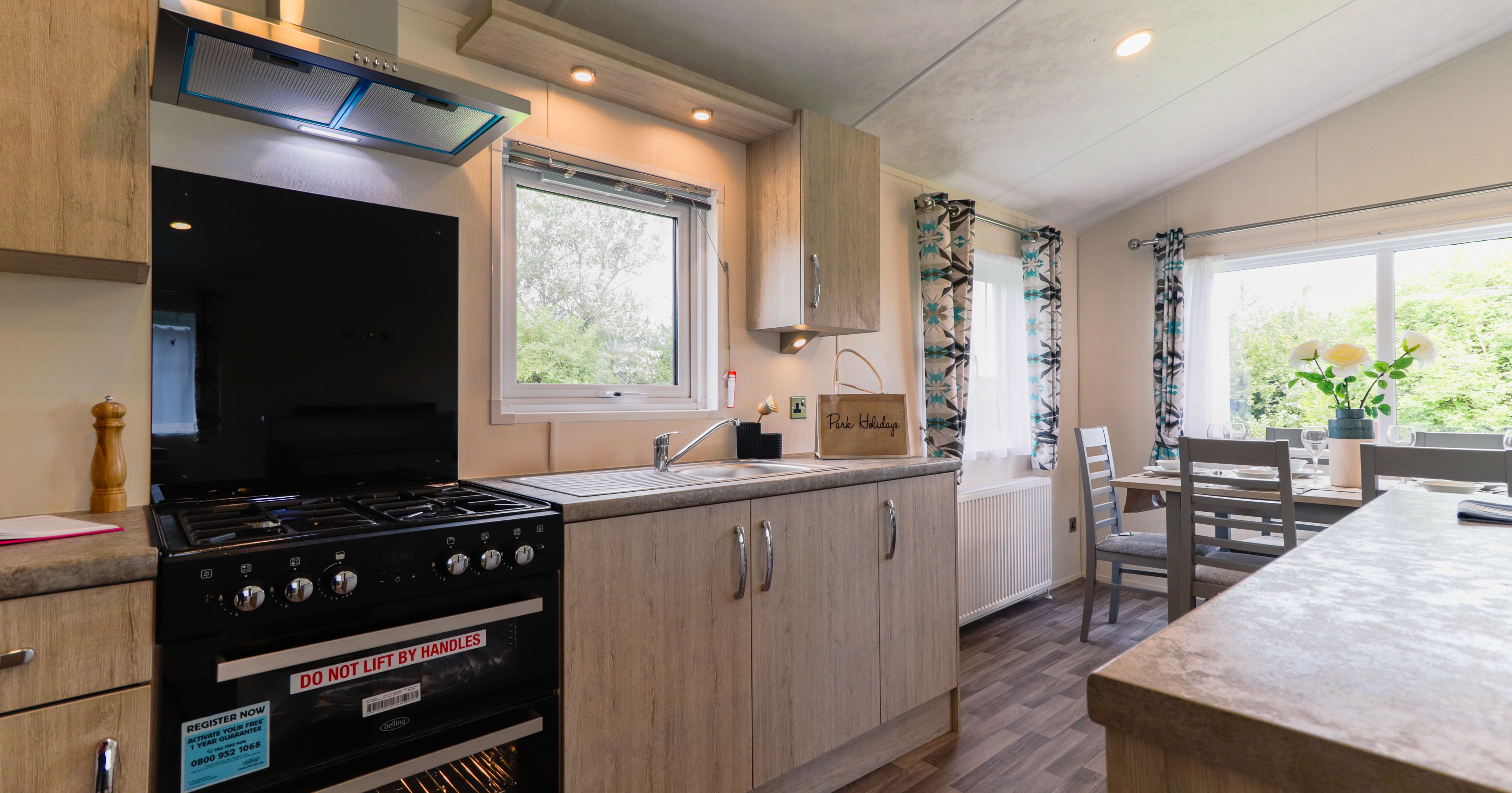 Modern kitchen with black cooker, wooden cabinets, sink and a small dining table by a bright window