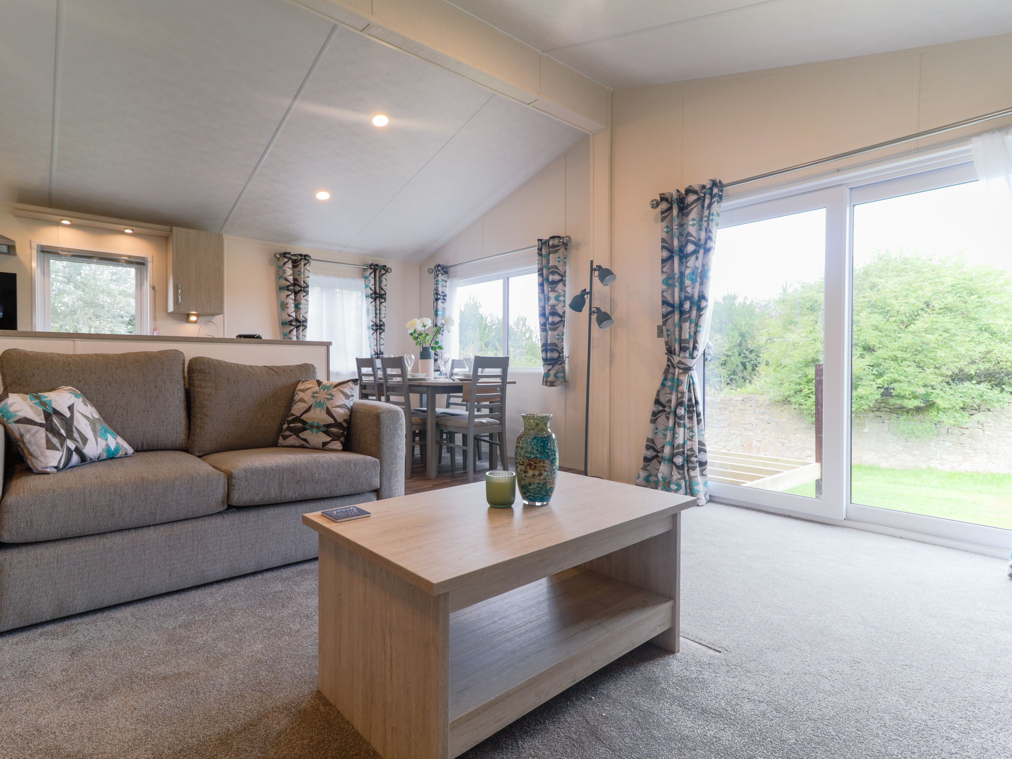 Modern open-plan living area with grey sofa, wooden coffee table, dining table and large sliding glass doors