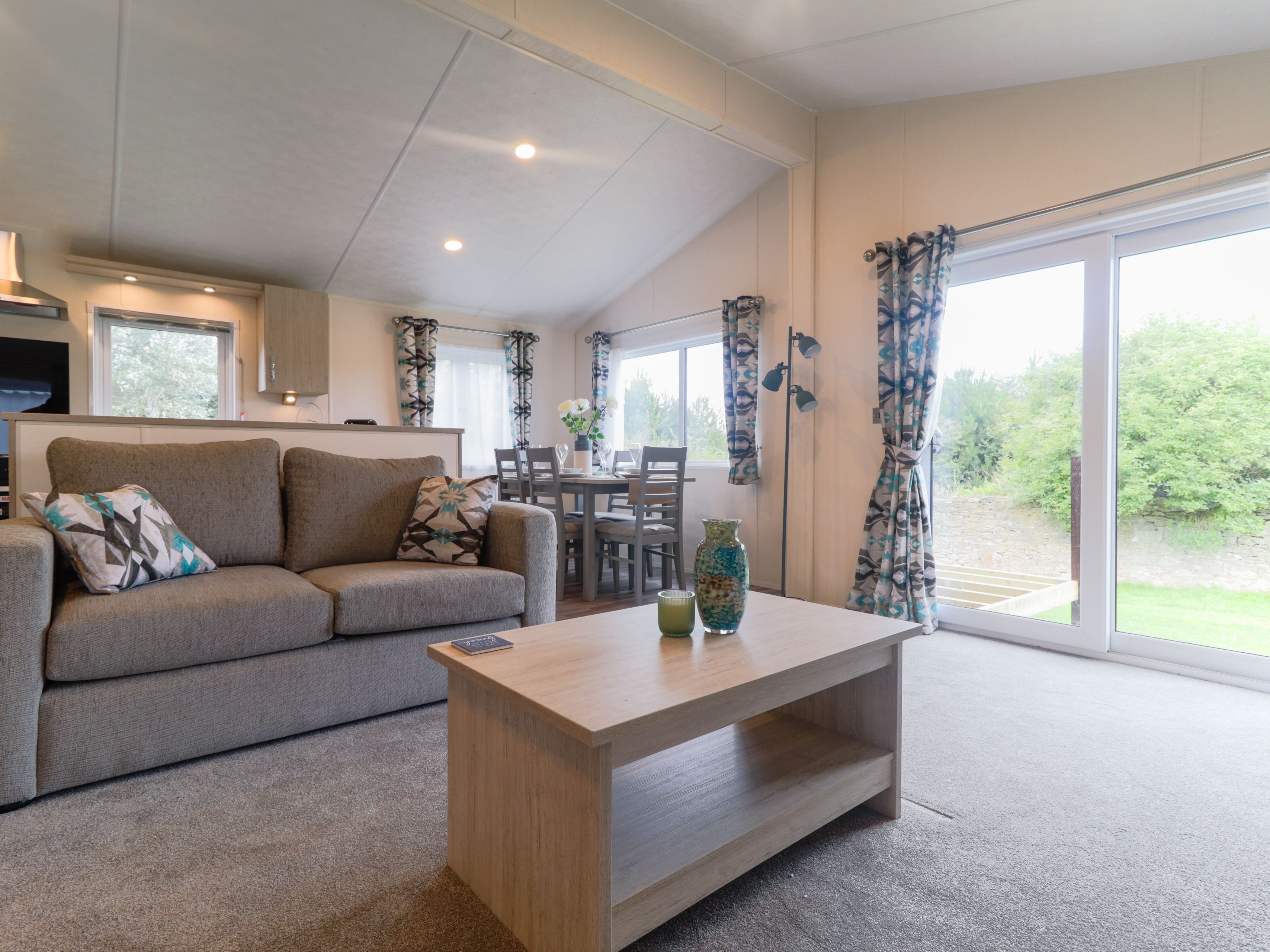 Modern open-plan living area with grey sofa, wooden coffee table, dining table and large sliding glass doors