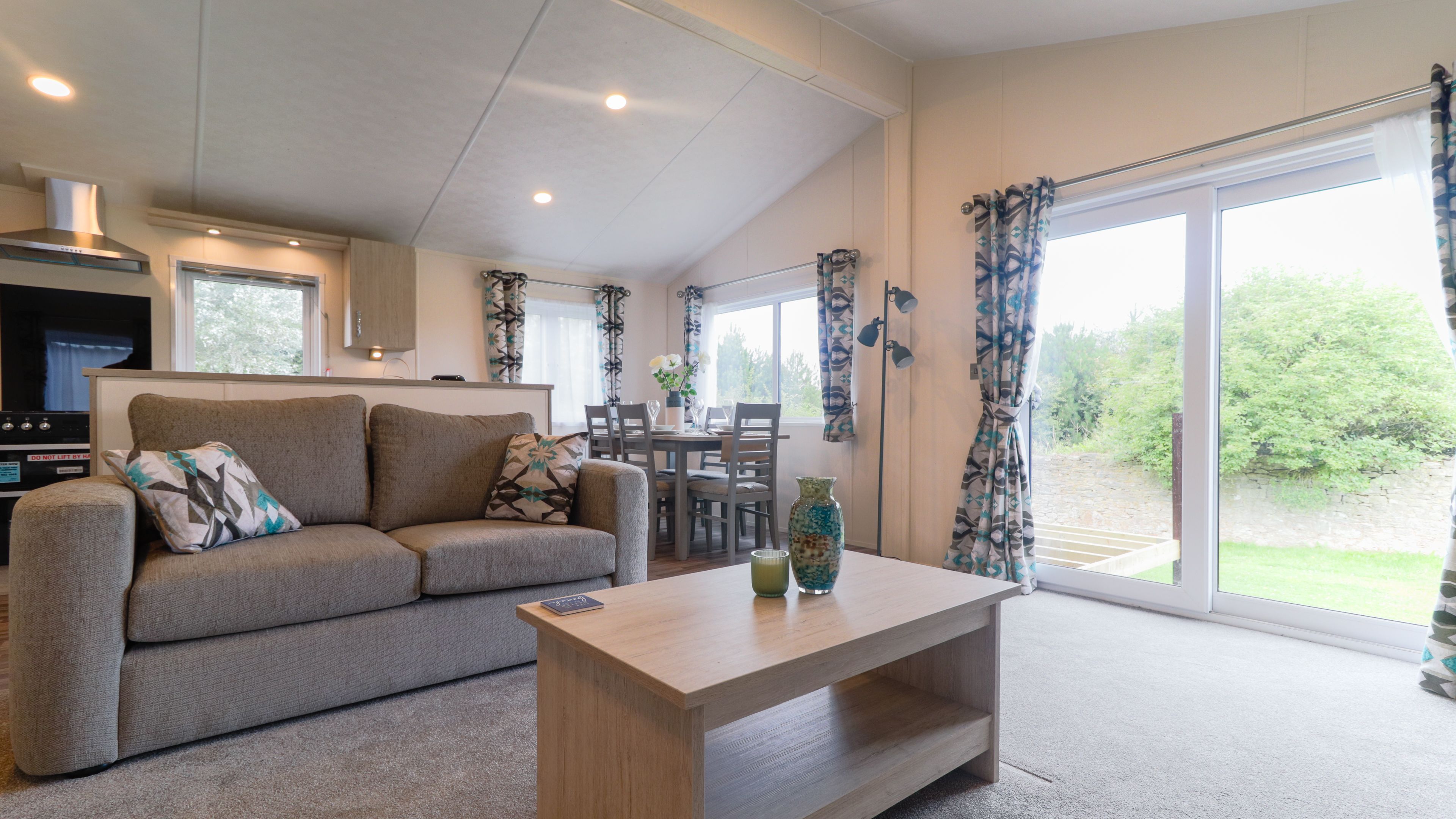 Modern open-plan living area with grey sofa, wooden coffee table, dining table and large sliding glass doors