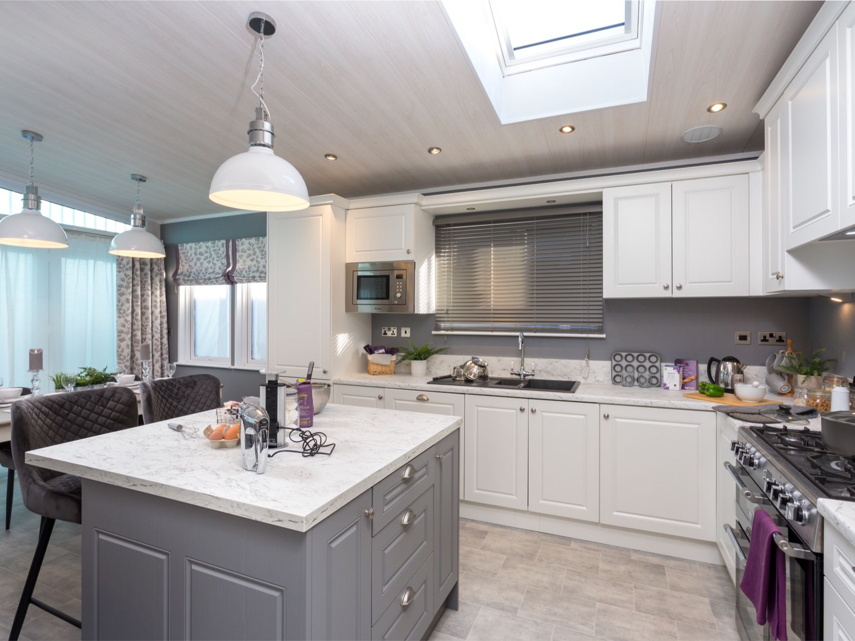 Modern kitchen with white cabinets, grey island and pendant lights under a skylight