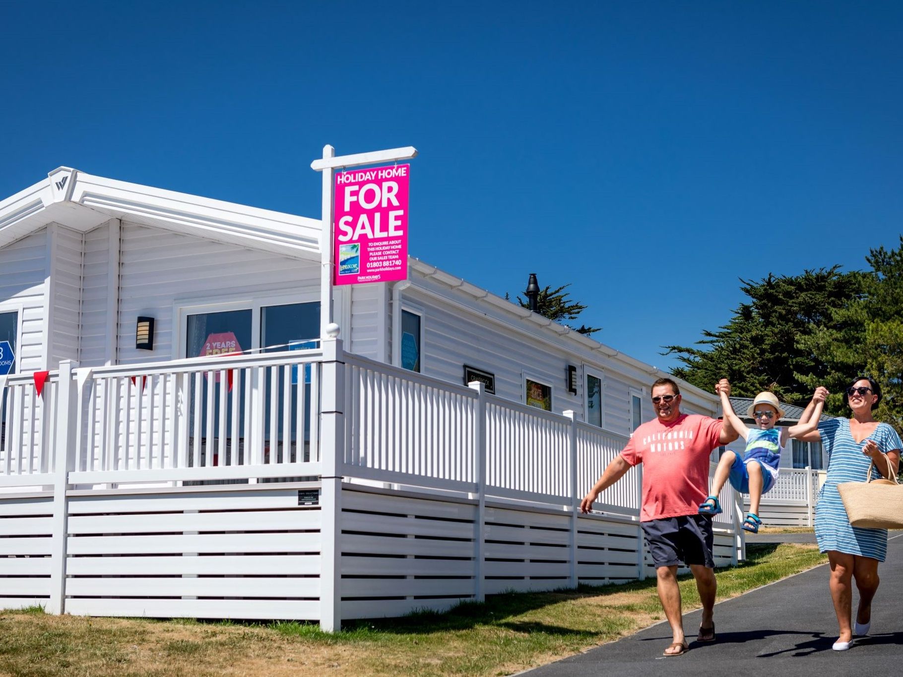 Family walking past a white holiday home with a 'For Sale' sign at Landscove Holiday Park