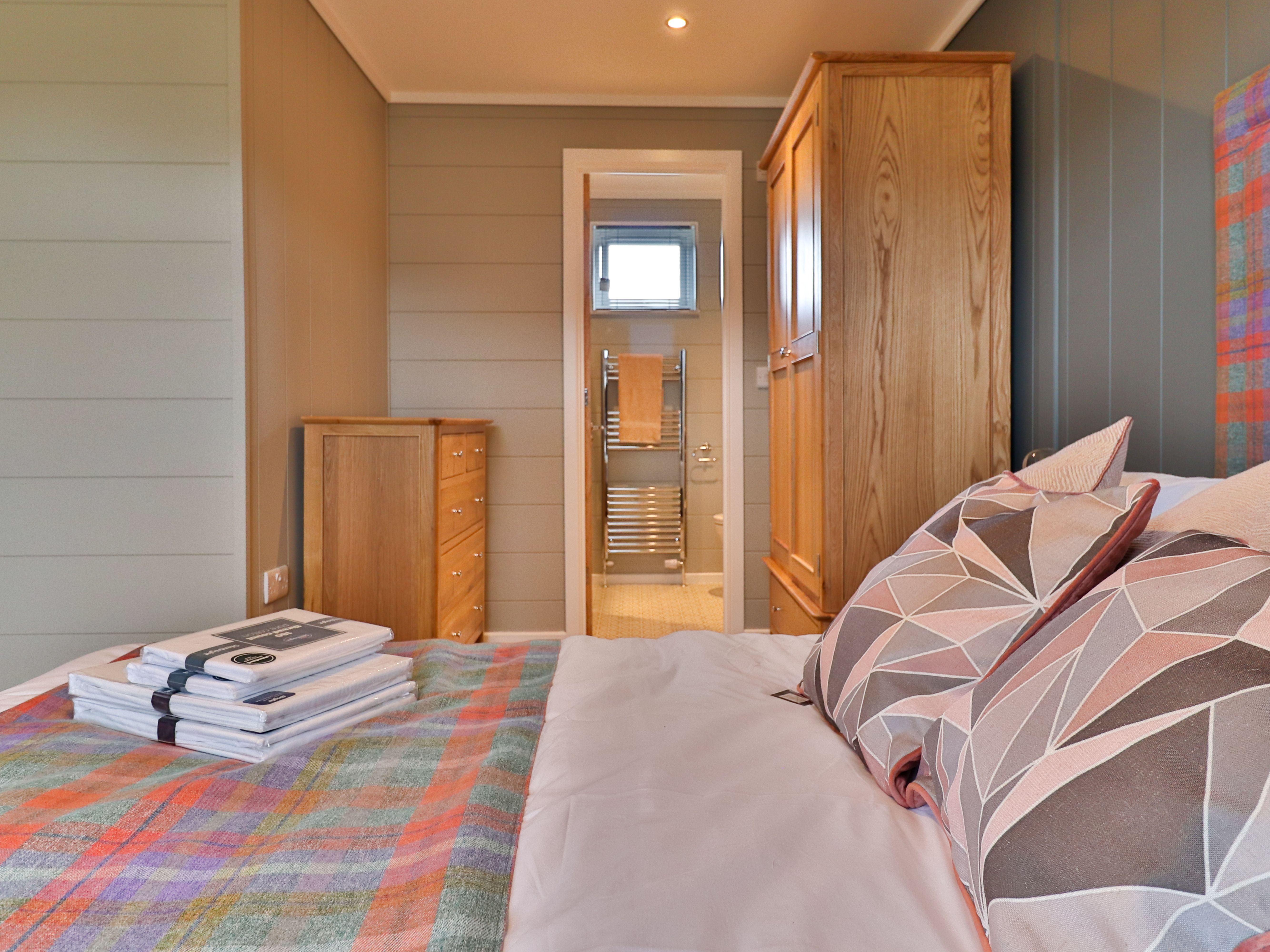 Cosy bedroom with double bed, patterned cushions and wooden wardrobe, looking through to an en-suite bathroom