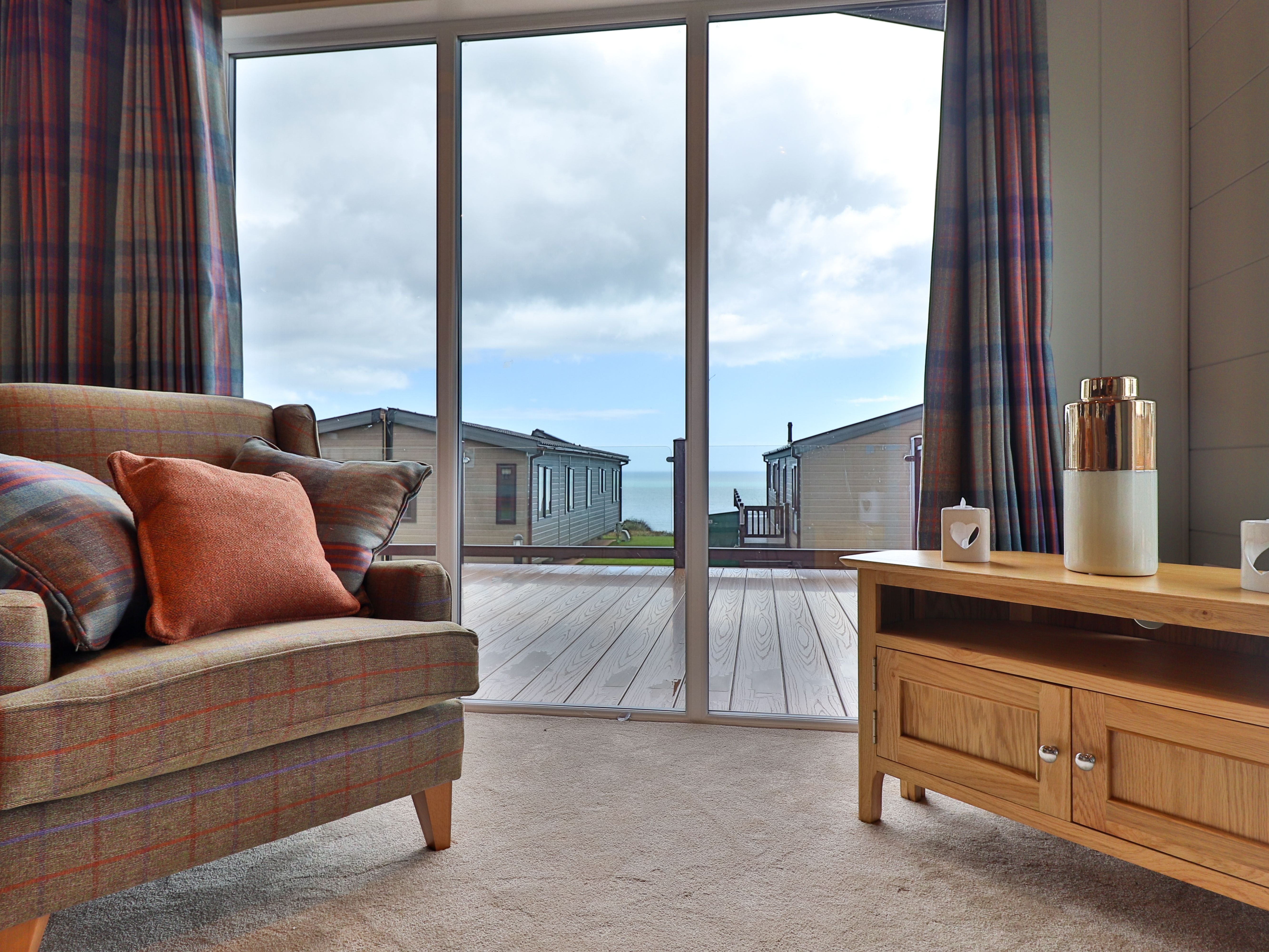 Cosy living room with armchair and wooden TV unit facing large glass doors to a seaside deck