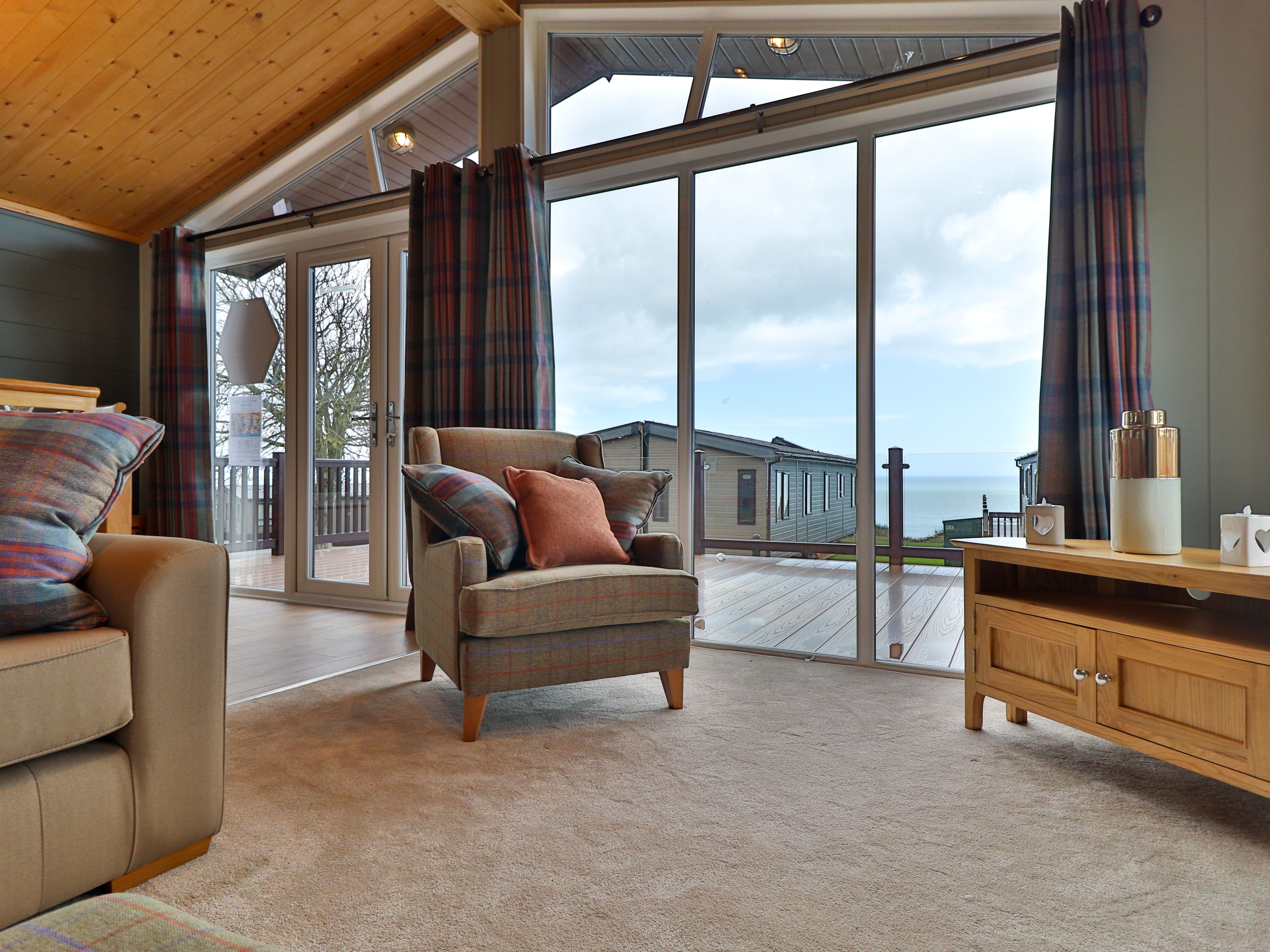 Cosy living room with armchair, sofa and large glass doors overlooking a deck and sea view