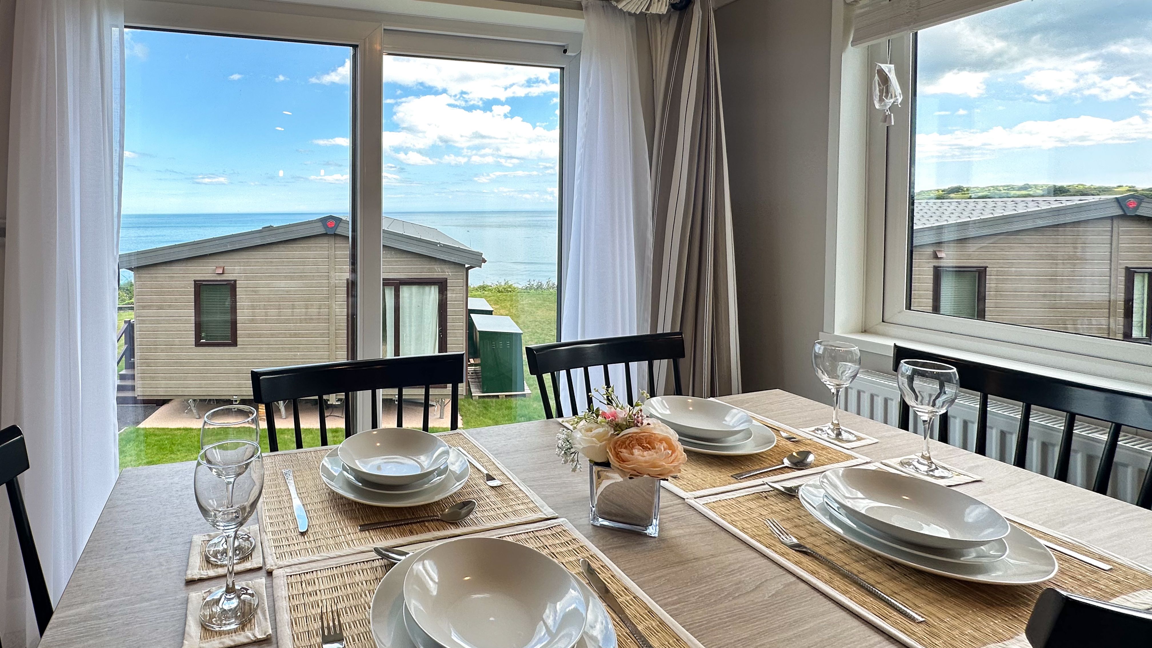 Set dining table by large windows with sea view beyond holiday lodges