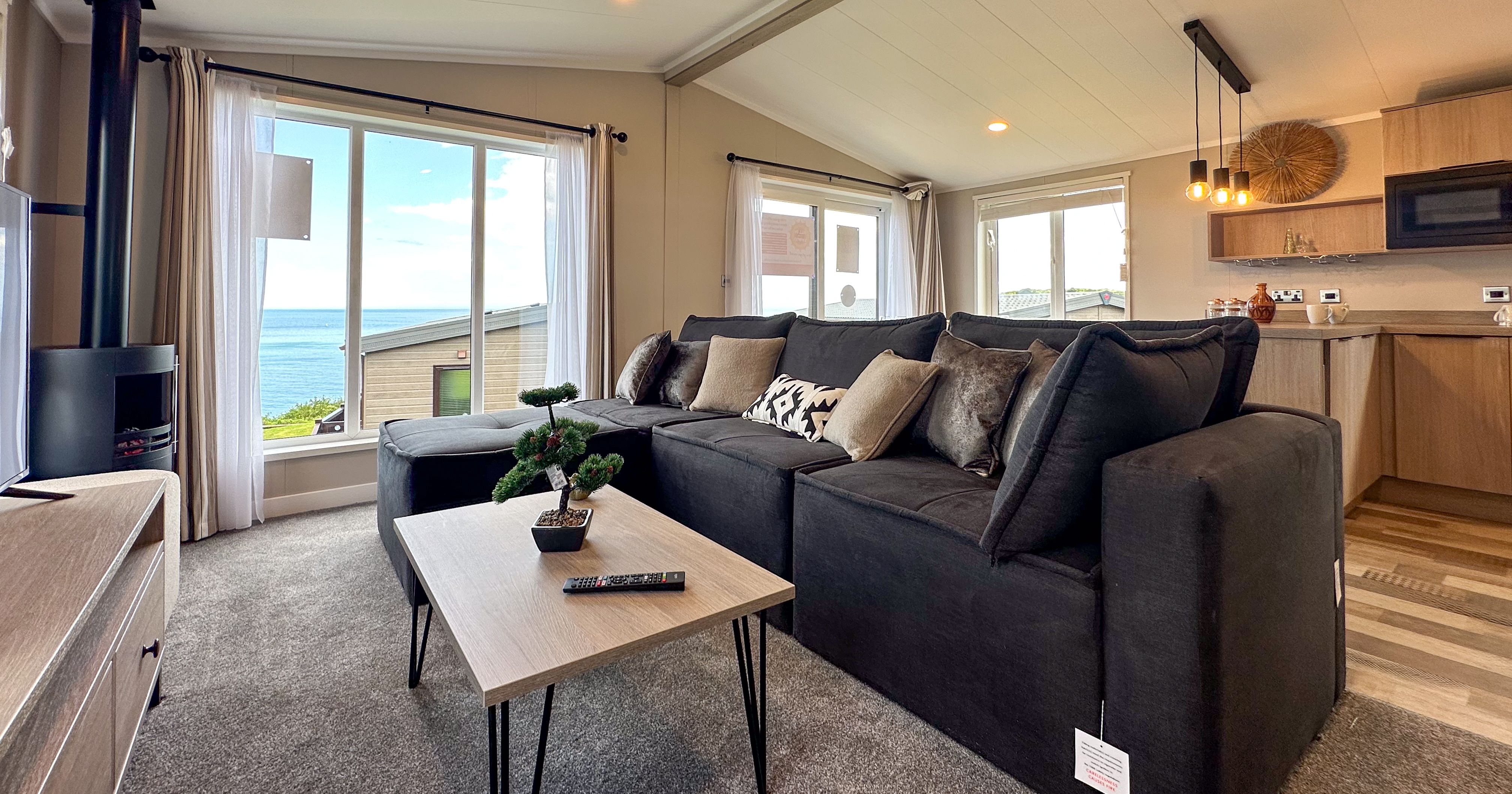 Modern open-plan living room with dark sectional sofa and large windows overlooking the sea