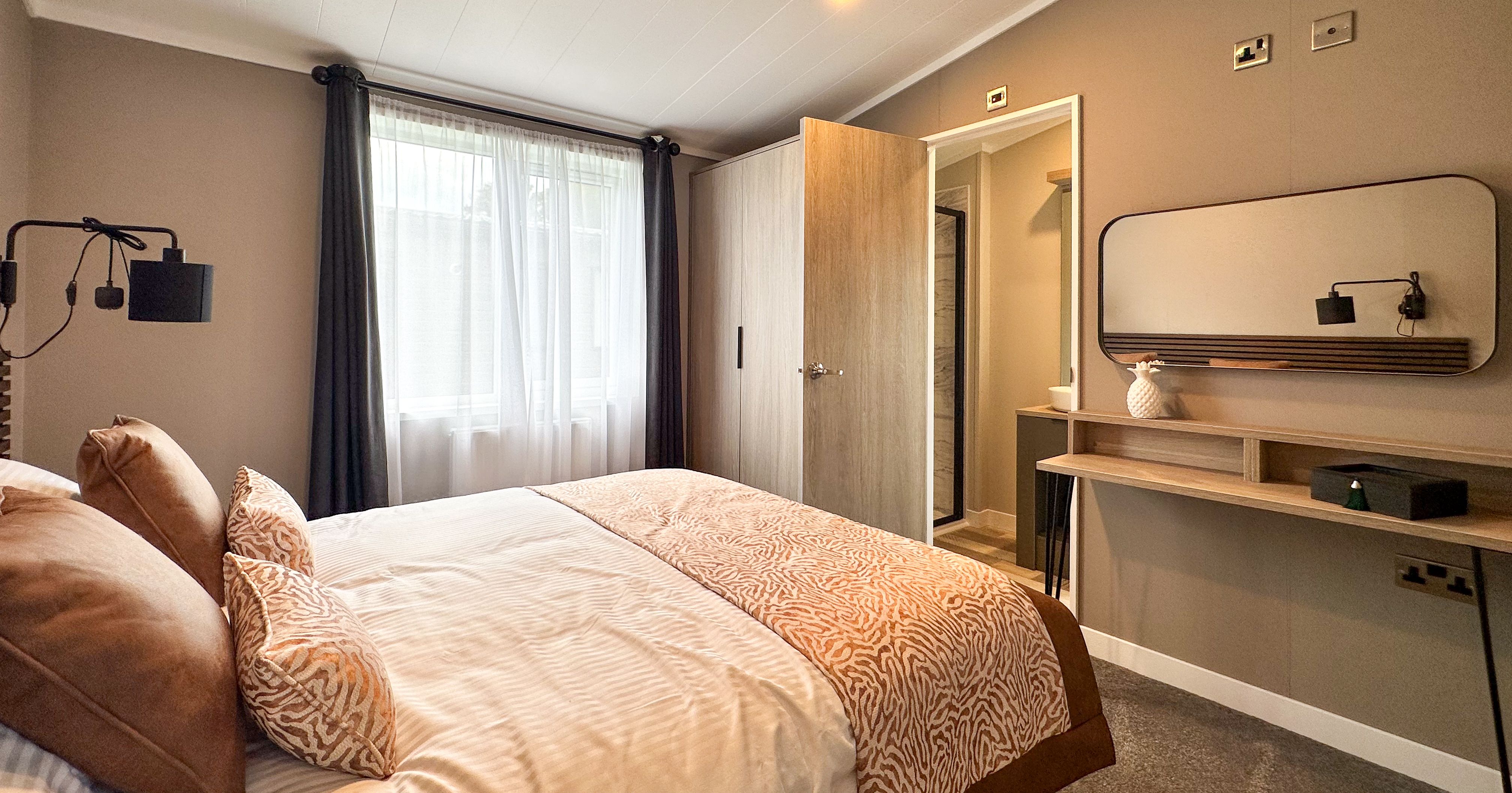 Modern bedroom with double bed, grey walls, window with dark curtains, and vanity desk with mirror
