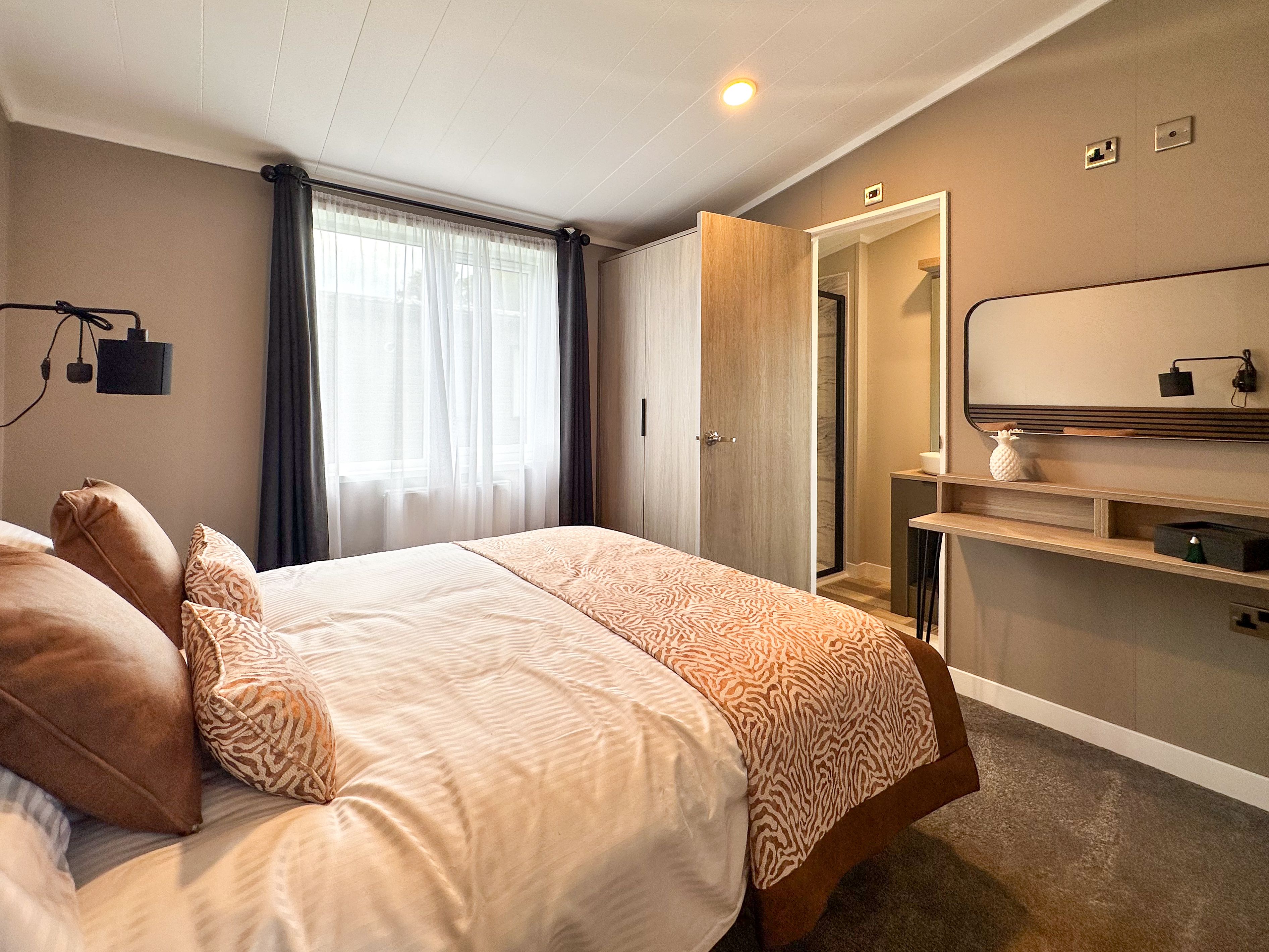 Modern bedroom with double bed, grey walls, window with dark curtains, and vanity desk with mirror