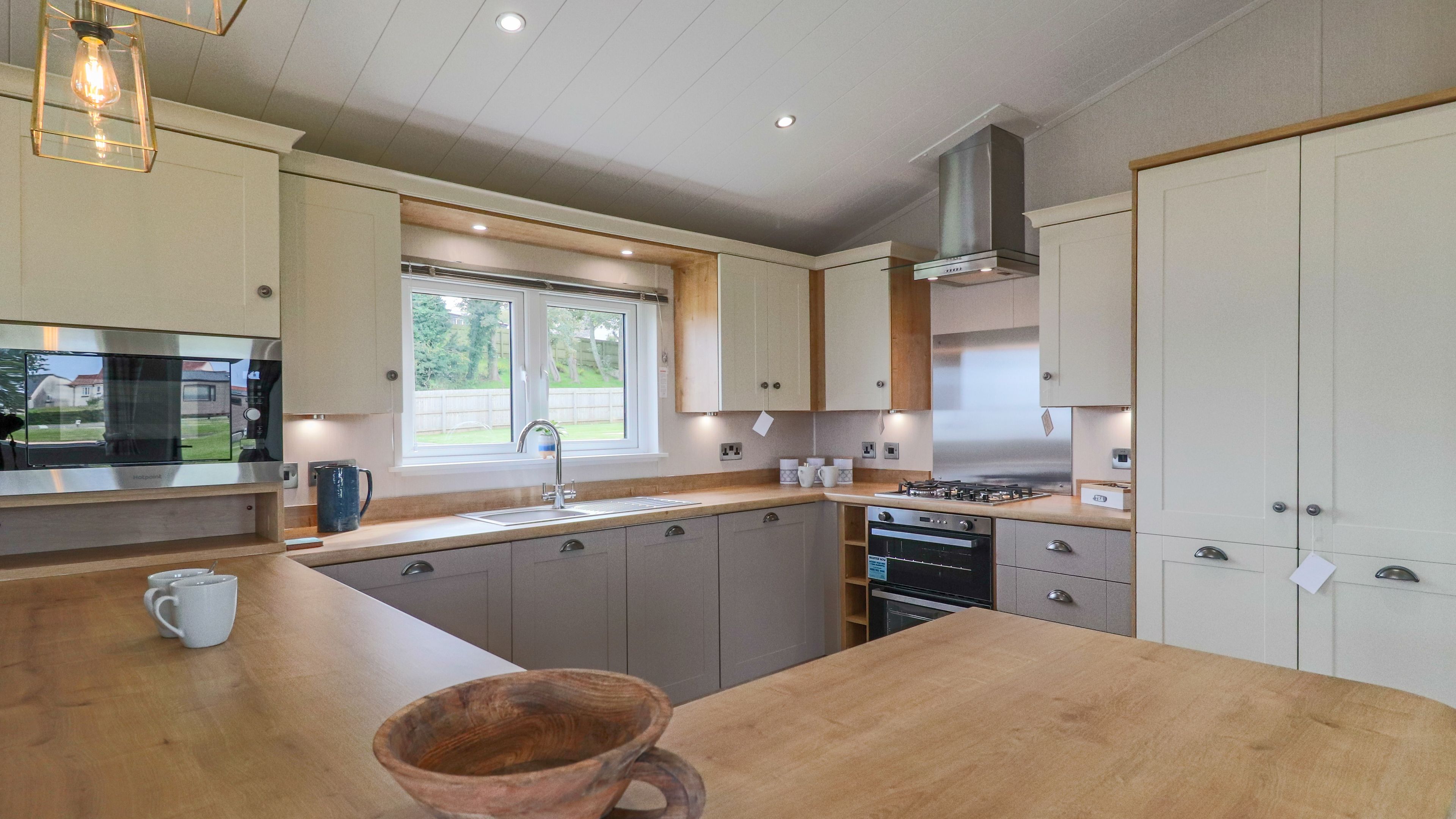 Modern fitted kitchen with wooden worktops, cream and grey cabinets, and a window above the sink