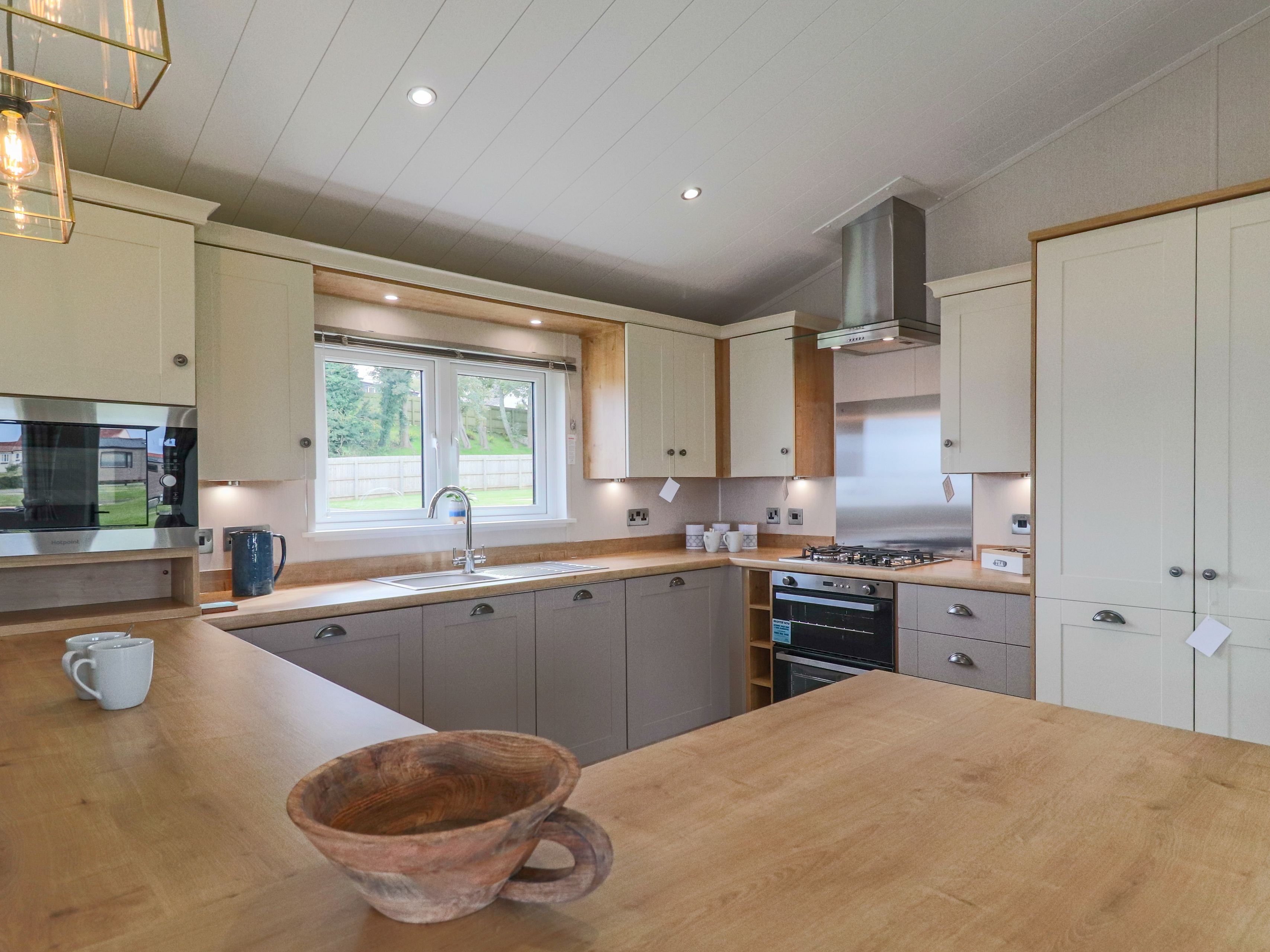 Modern fitted kitchen with wooden worktops, cream and grey cabinets, and a window above the sink