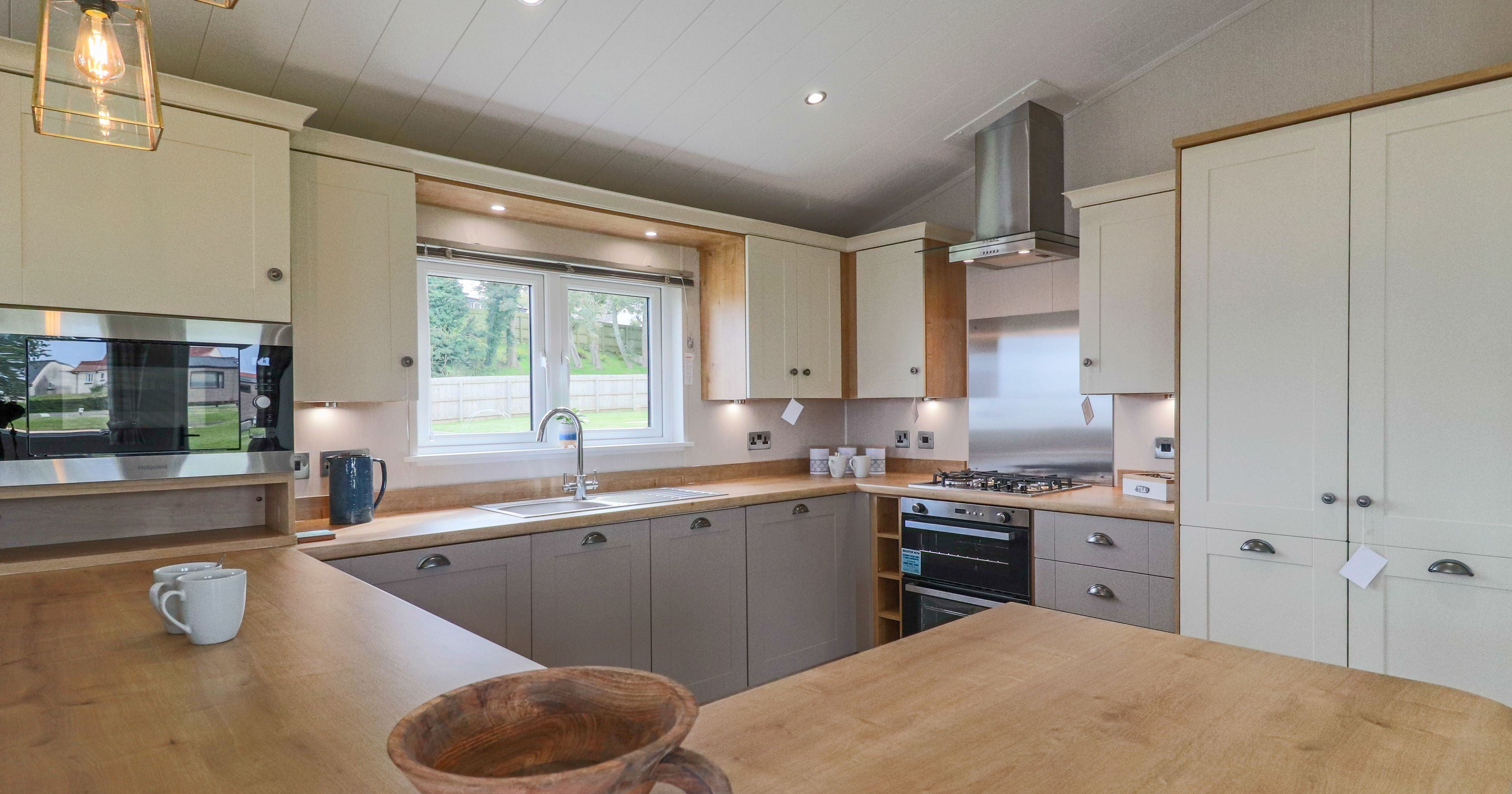 Modern fitted kitchen with wooden worktops, cream and grey cabinets, and a window above the sink