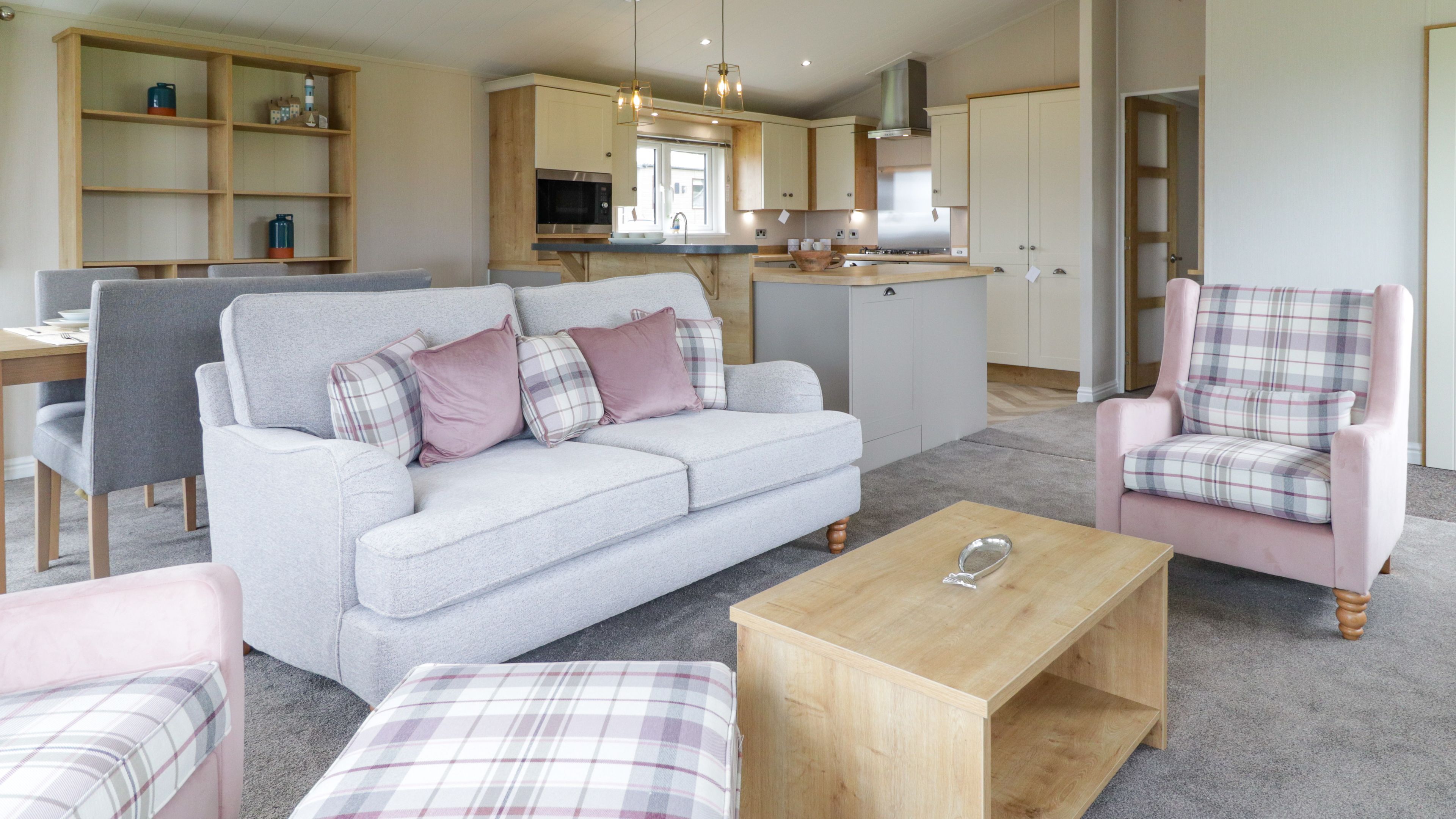 Modern open-plan living room and kitchen with grey sofa, pink plaid armchairs and wooden coffee table