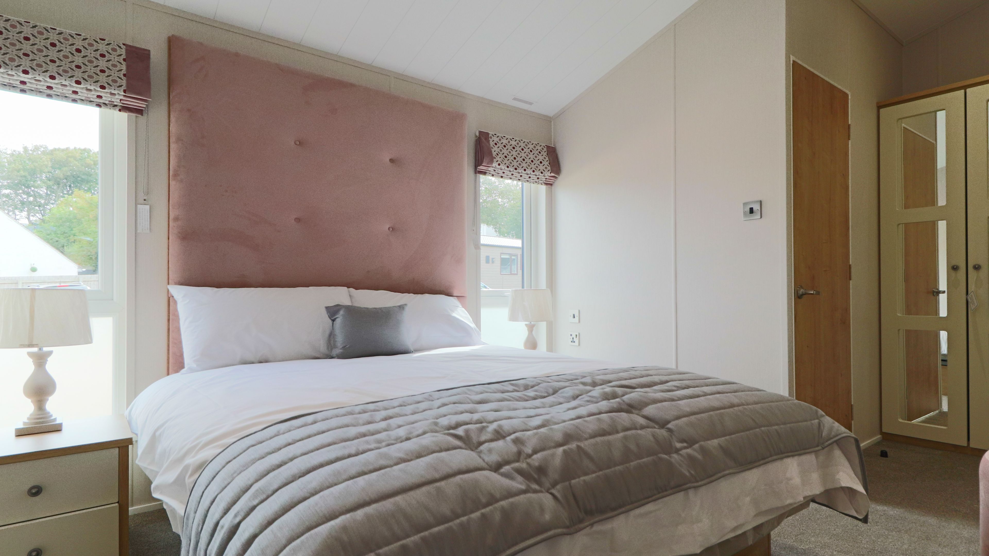 Bright bedroom with double bed, pink upholstered headboard, bedside lamps and mirrored wardrobe