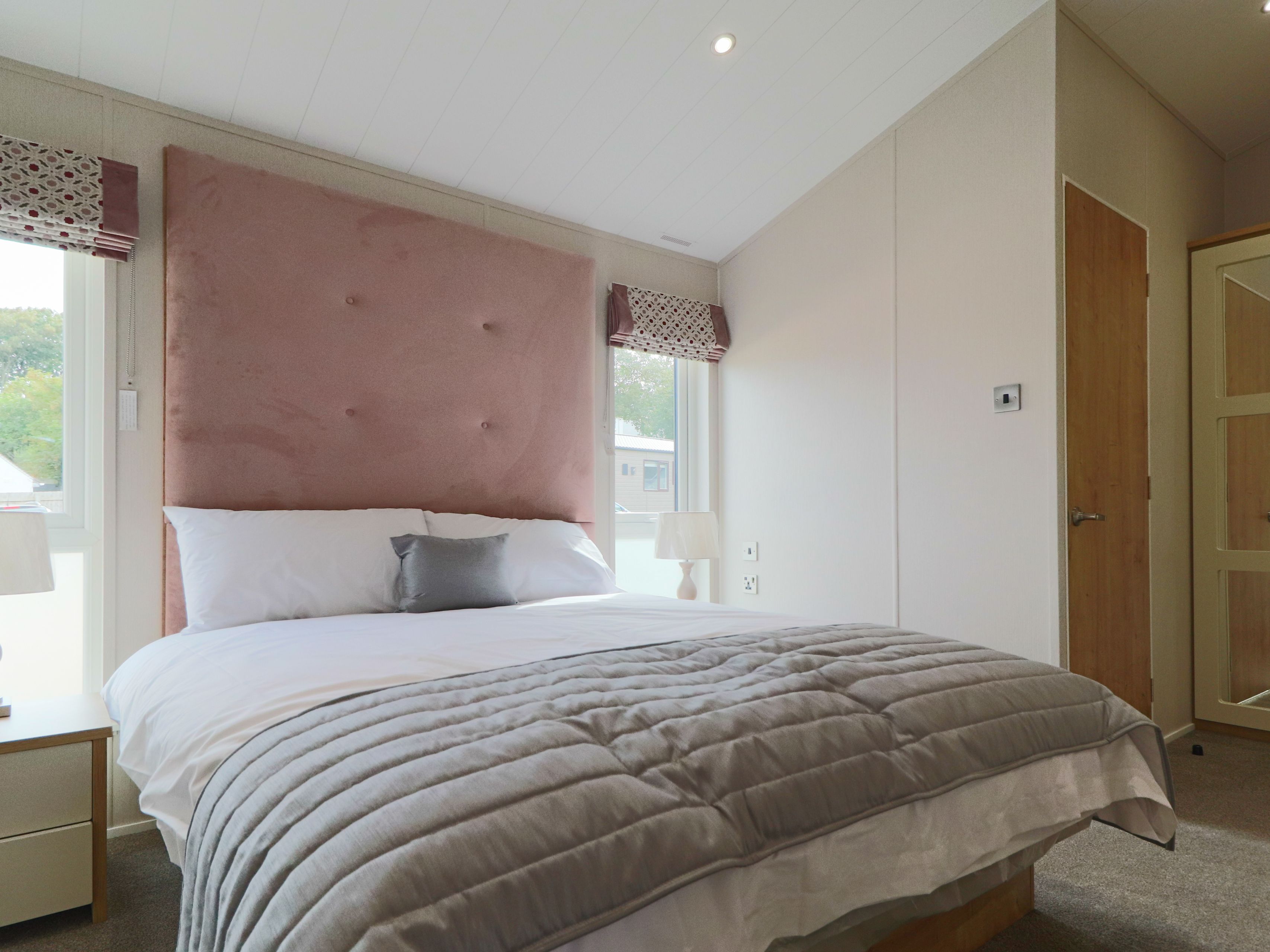 Bright bedroom with double bed, pink upholstered headboard, bedside lamps and mirrored wardrobe