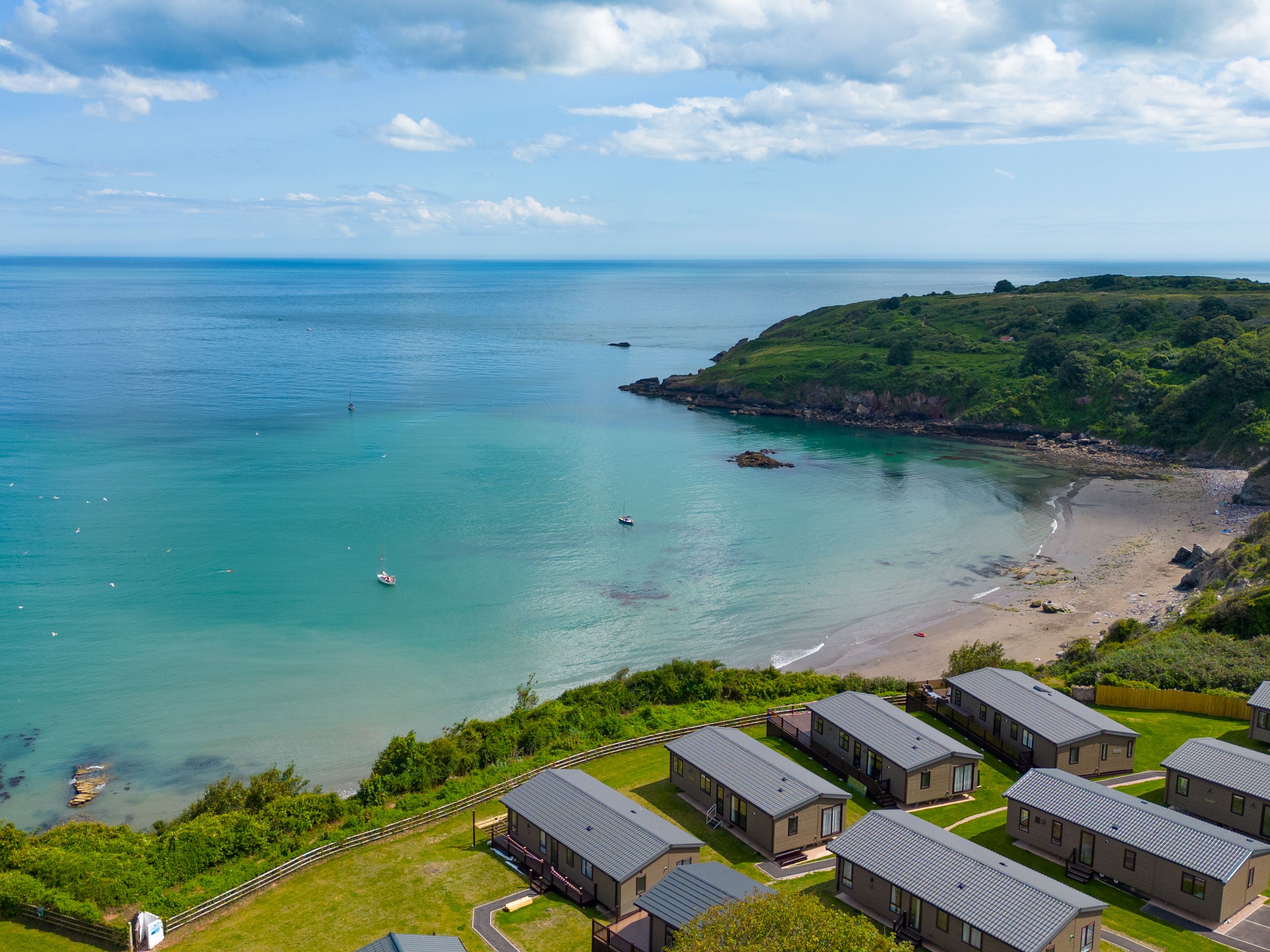 Aerial view of a turquoise bay with a sandy beach, small boats and coastal holiday lodges
