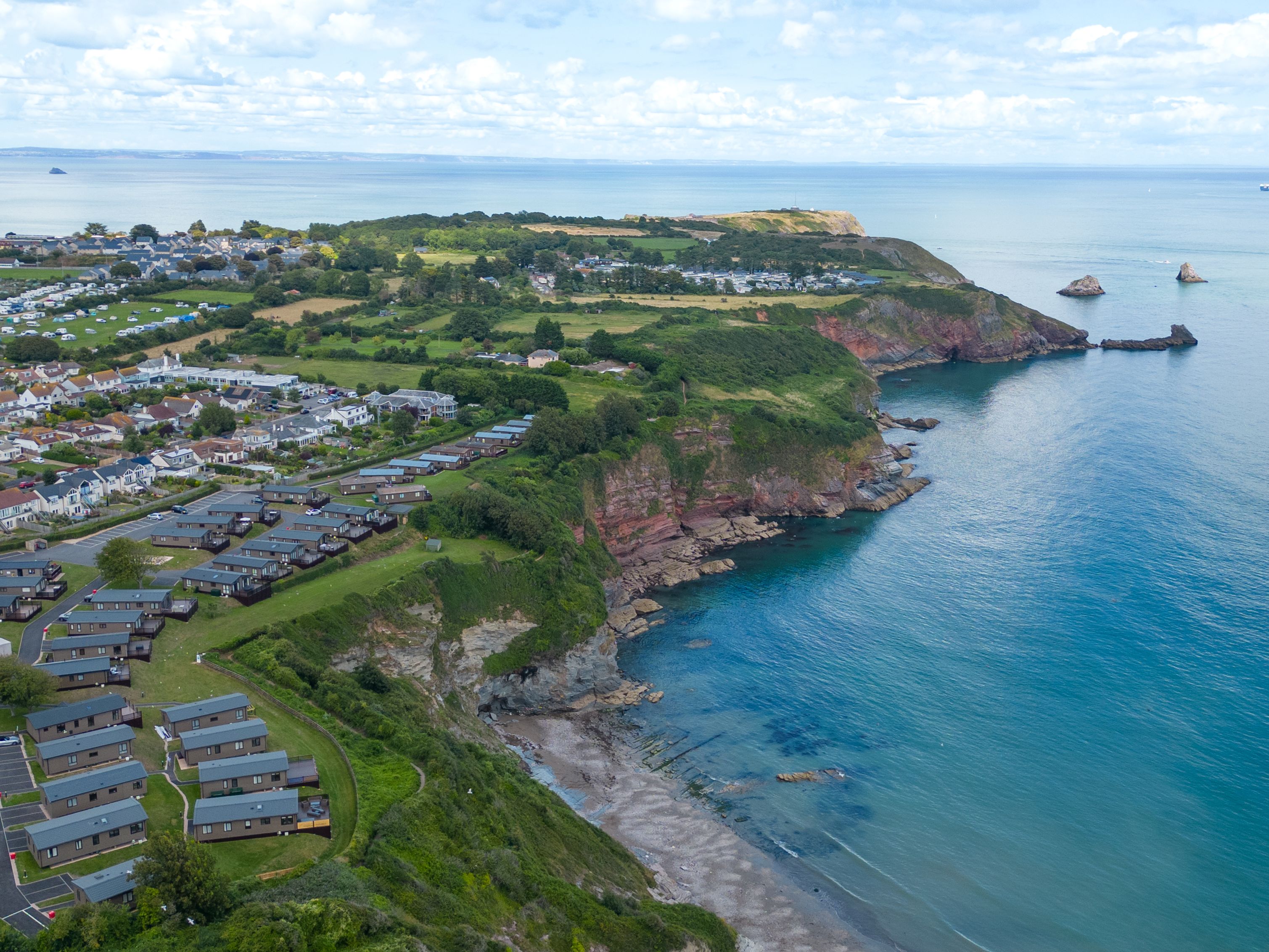 Aerial view of a coastal town beside green cliffs and a calm blue sea