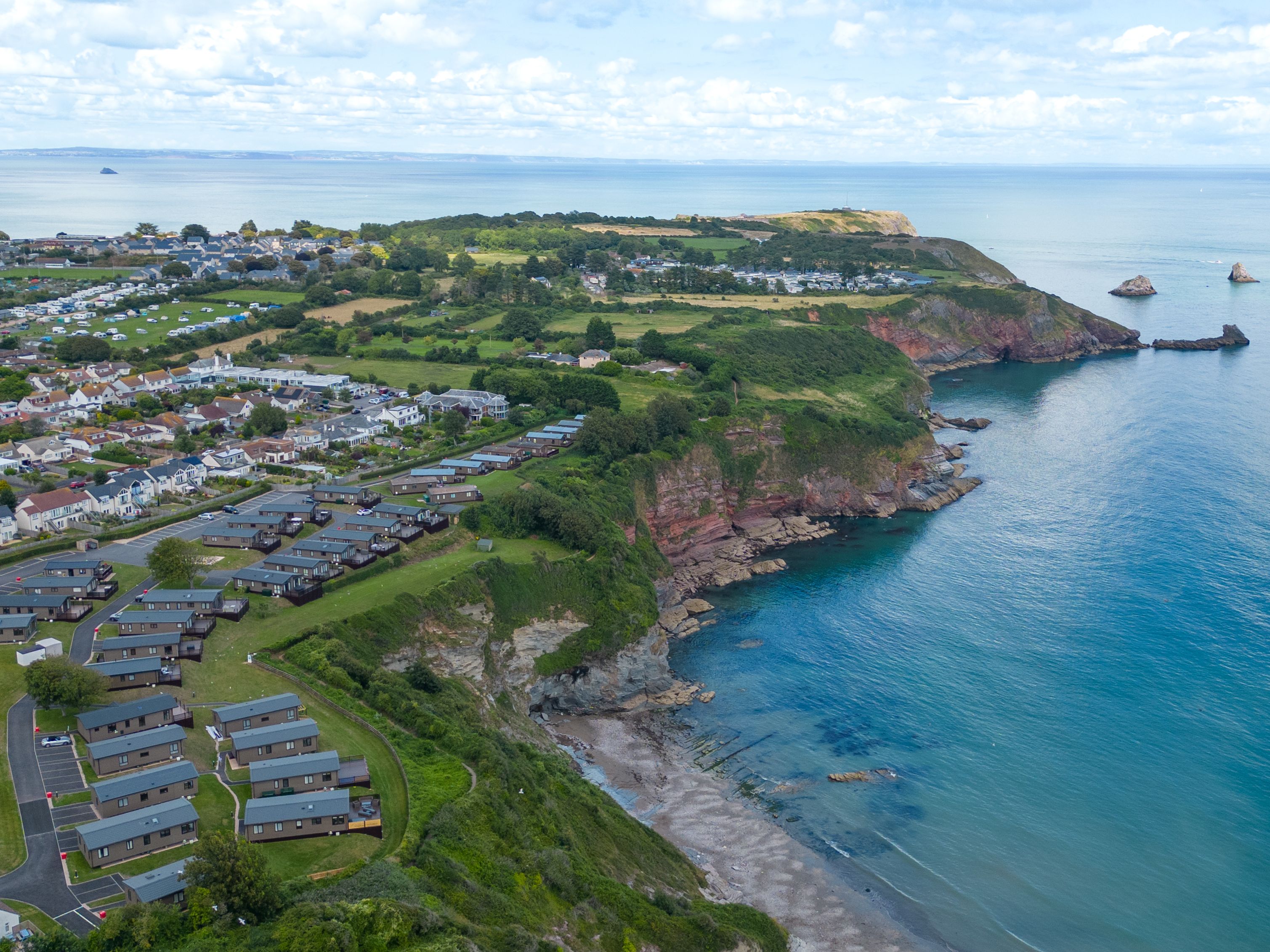 Aerial view of a coastal town beside green cliffs and a calm blue sea