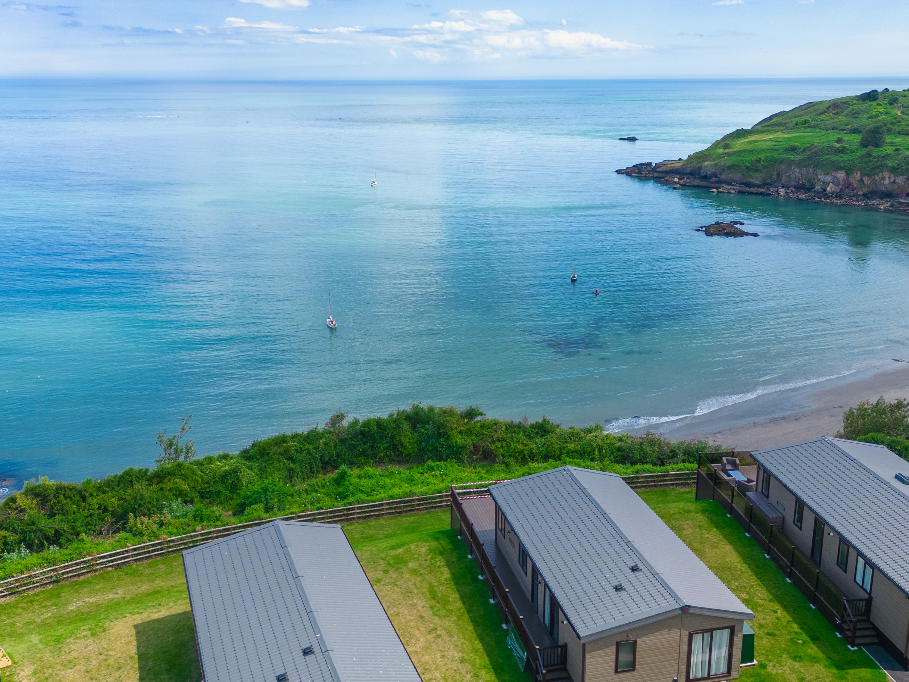 Coastal bay with calm blue sea, sandy beach, green headland and holiday lodges in the foreground