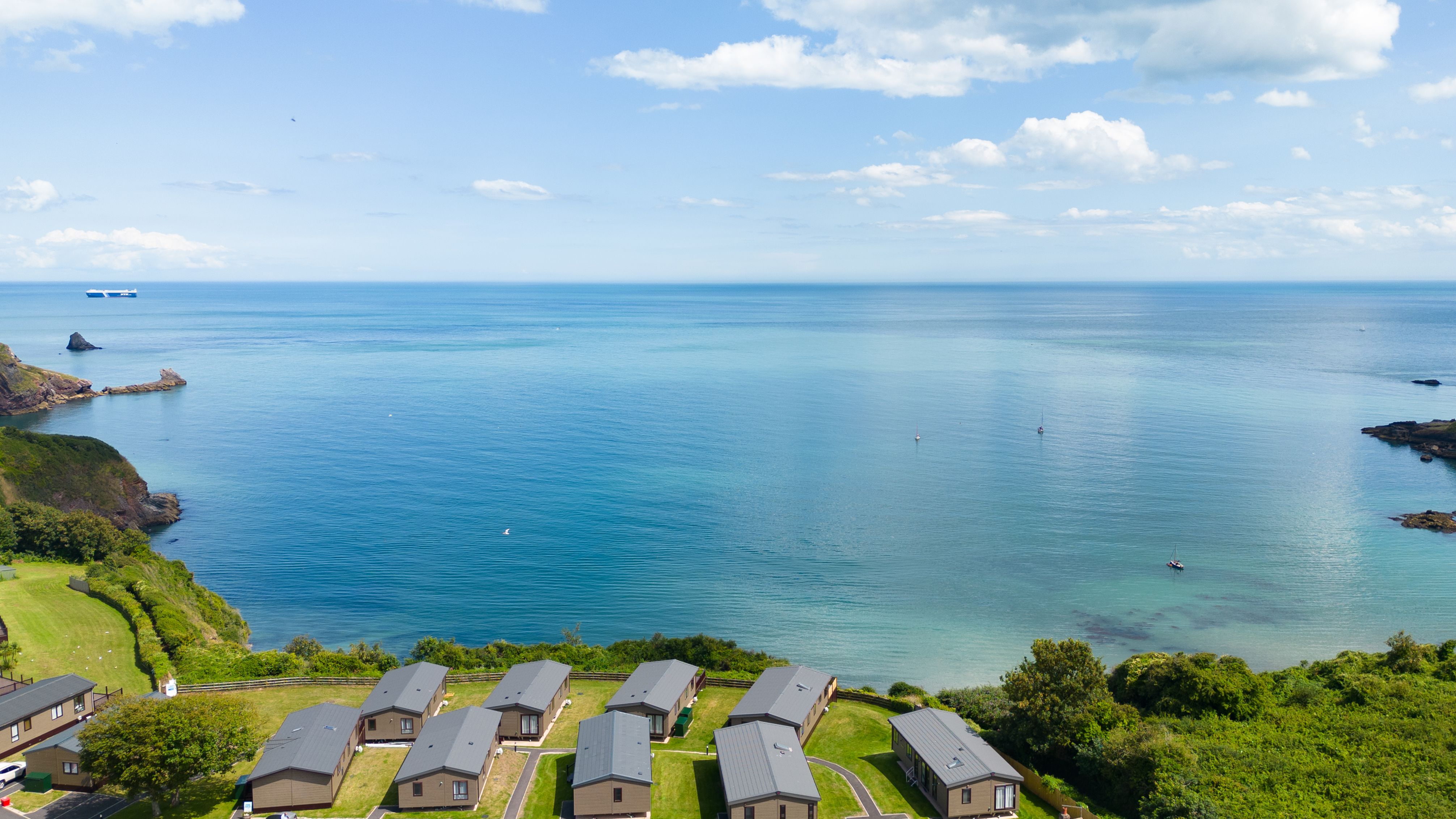 Coastal holiday lodges overlooking a calm blue sea under a partly cloudy sky