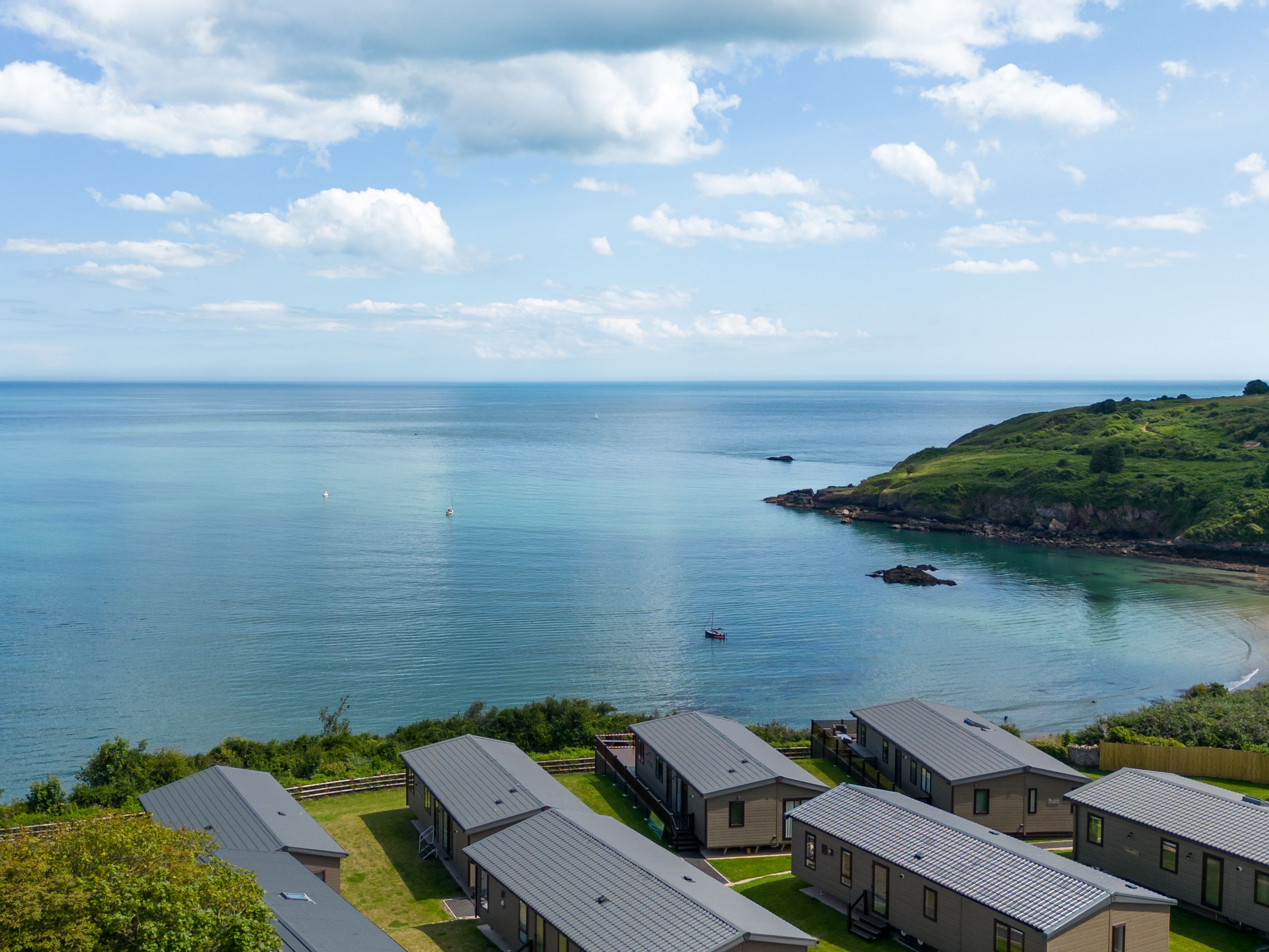 Coastal holiday park with caravans overlooking a calm blue sea and green headland under a partly cloudy sky