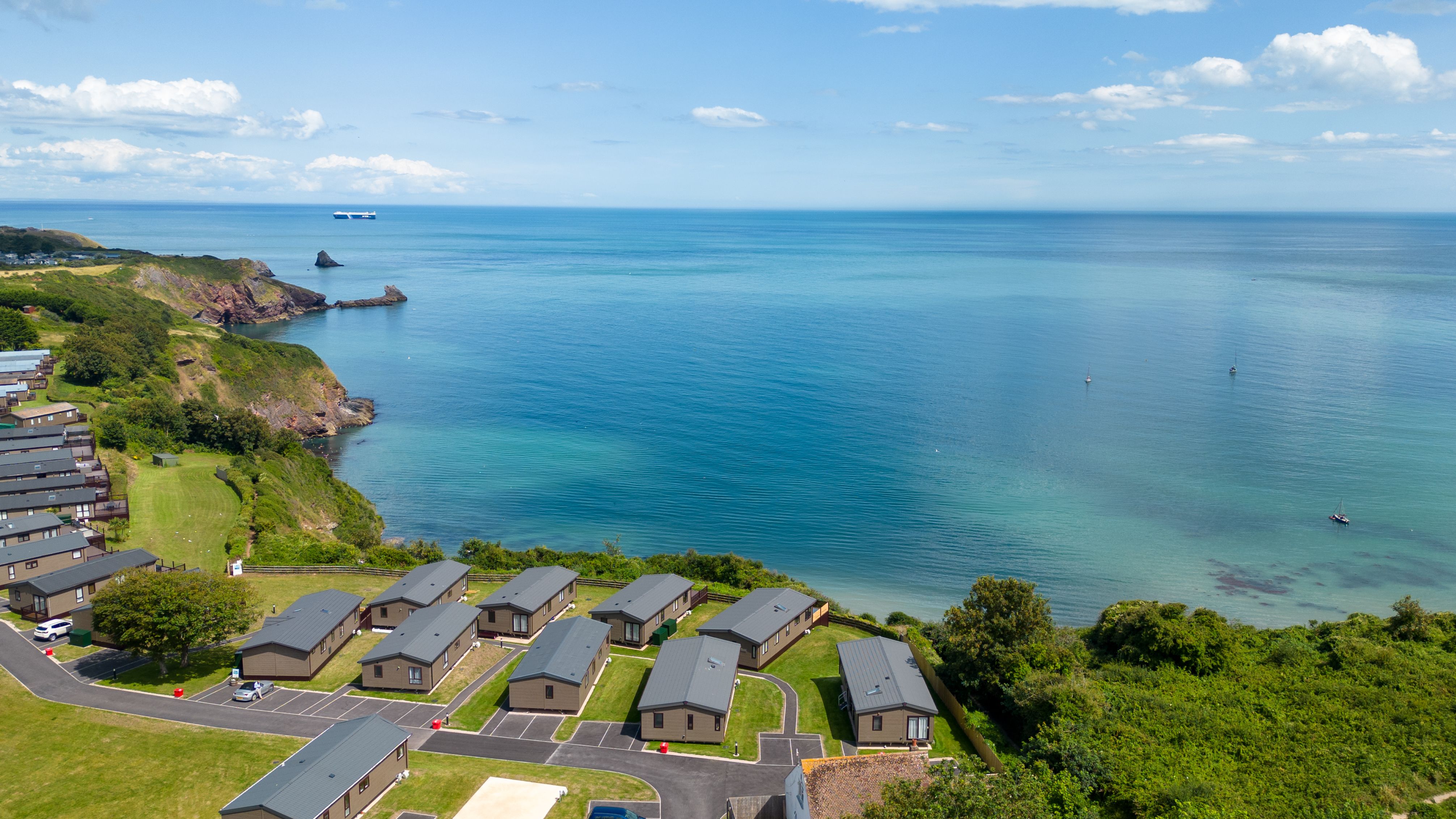 Coastal holiday park cabins overlooking a calm blue sea and rocky headland