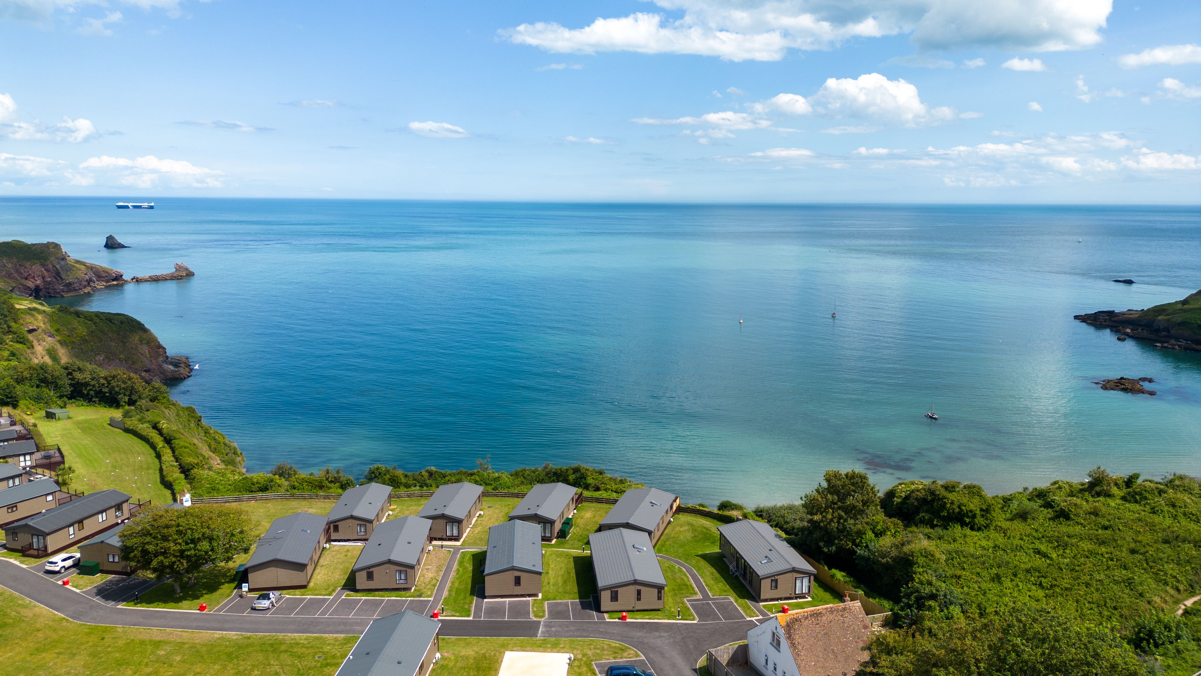 Coastal holiday park lodges overlooking a calm blue sea and cliffs under a partly cloudy sky