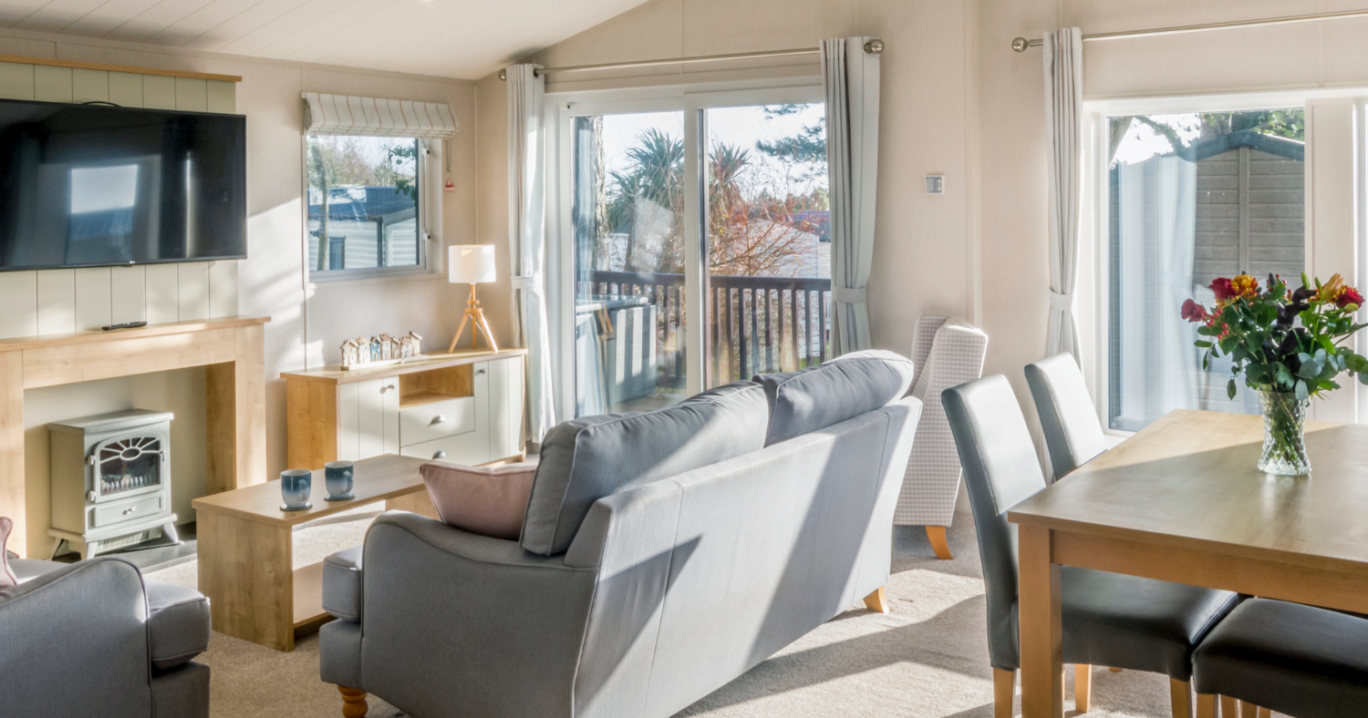 Bright, modern living and dining area with sofas, a wall-mounted television, and large glass doors leading to a deck
