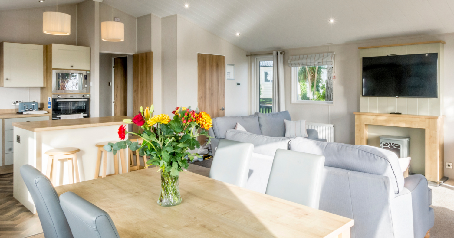 Bright open-plan living room and kitchen with dining table, grey sofas and wall-mounted TV