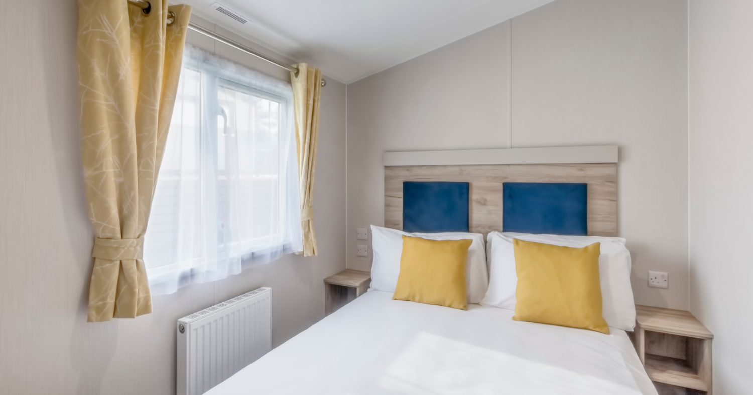 Bright double bedroom with white bedding, blue headboard panels and yellow cushions beside a window with yellow curtains.