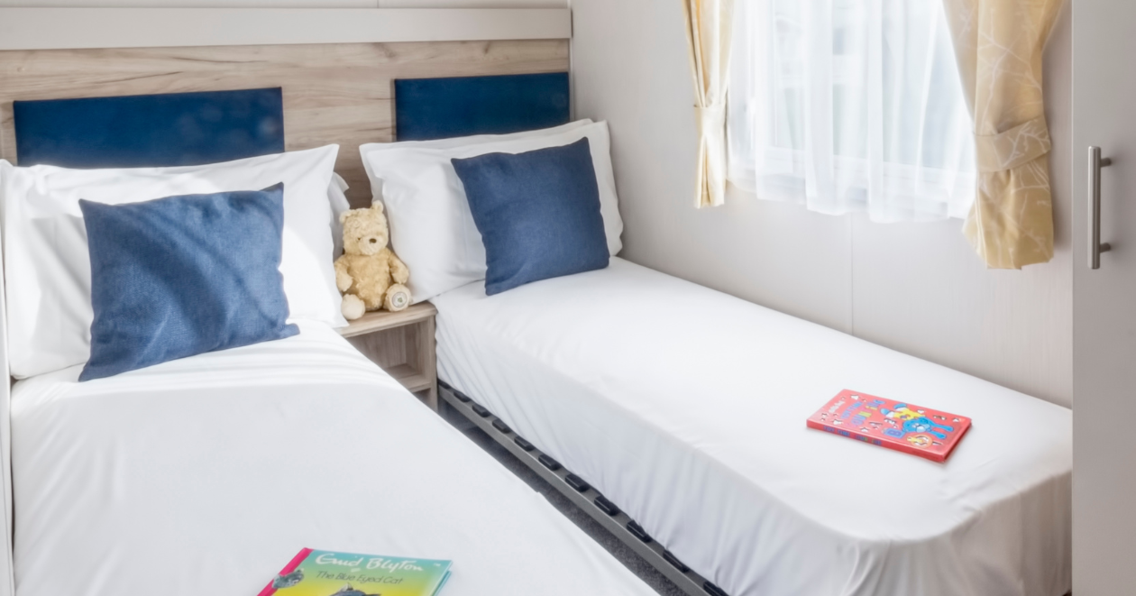 Bright twin bedroom with two single beds, blue cushions and a window with yellow curtains