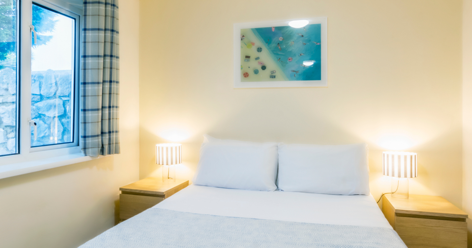 Cosy bedroom with a double bed, bedside lamps and a window with checked curtains