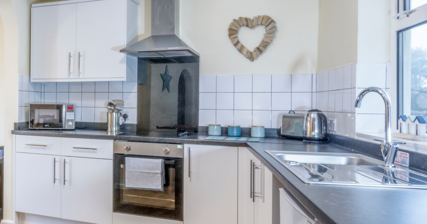 Modern white kitchen with stainless steel oven, hob, extractor and sink