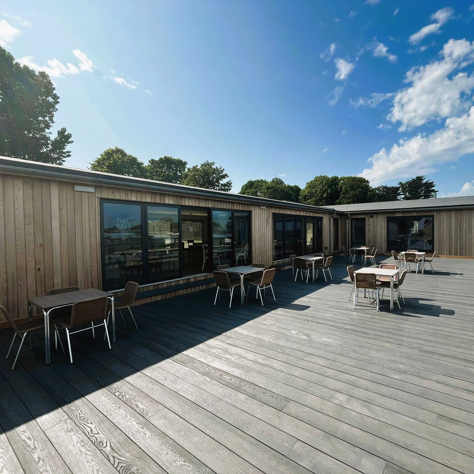 Outdoor terrace with tables and chairs beside a modern timber-clad building under a blue sky