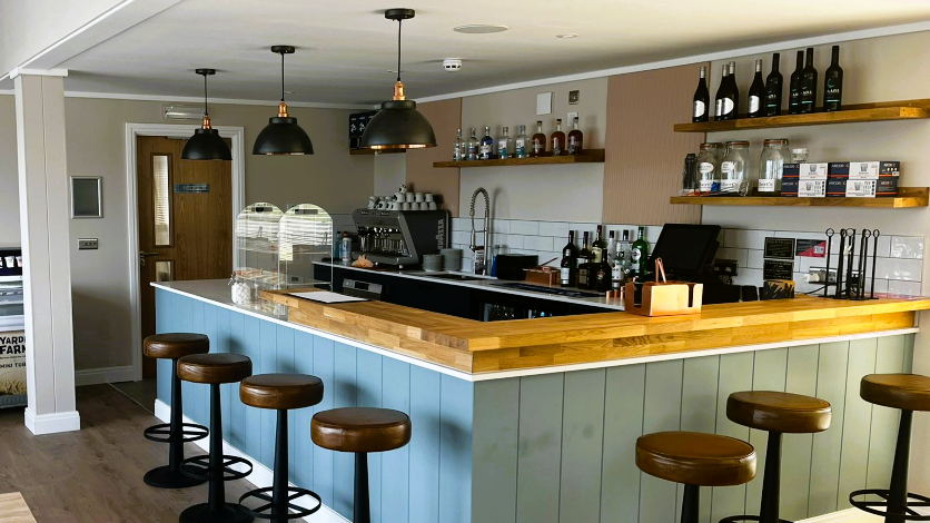 Modern bar interior with wooden countertop, pastel panelled bar front and leather bar stools under pendant lights